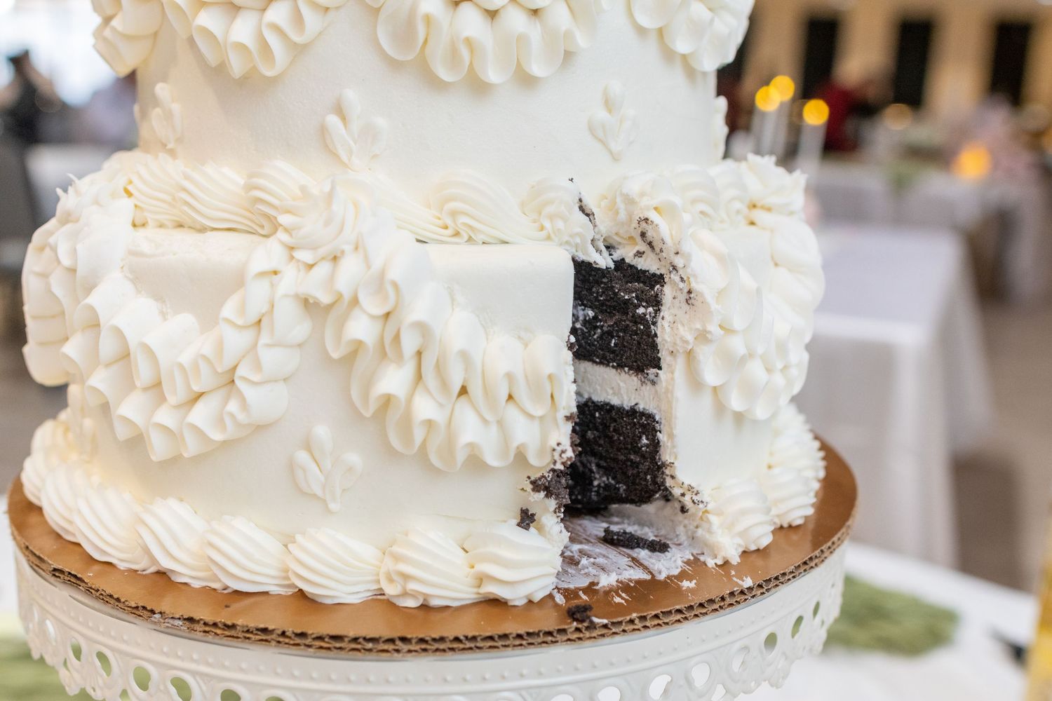 A white wedding cake decorated in vintage style with whipped white frosting and sits elegantly on a wooden stand.