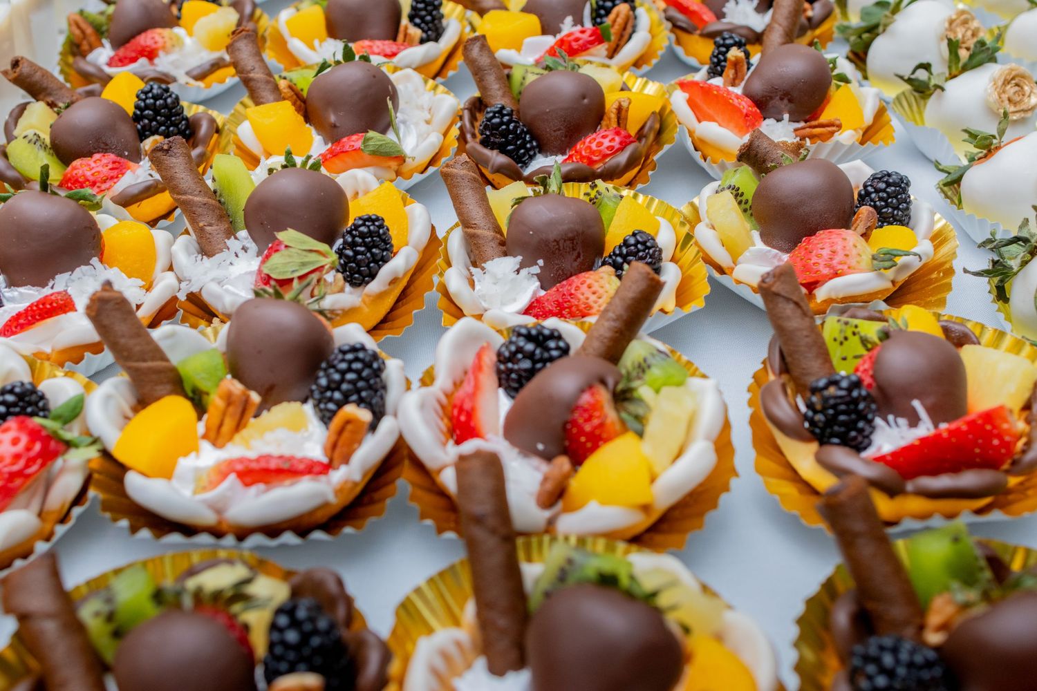 Decorative mini fruit tarts topped with chocolate and fresh berries displayed at a Quinlan, Texas mexican wedding dessert table