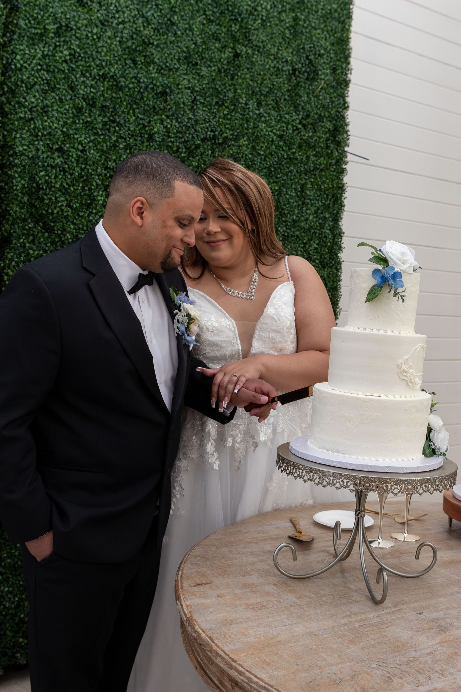 A bride and groom share an intimate moment while cutting their white wedding cake on a silver stand at the cinnamon barn wedding venue.