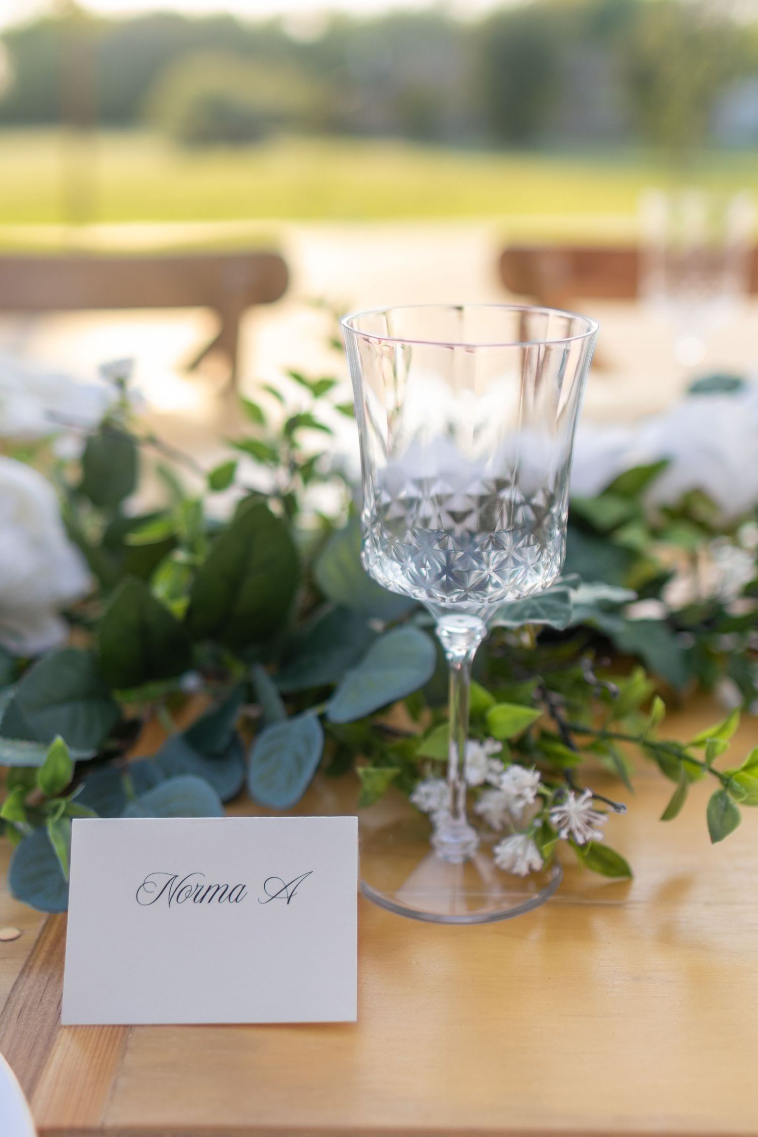 Elegant crystal wine glass and place setting, greenery and floral accents at a rustic wedding reception in East Texas, romantically styled