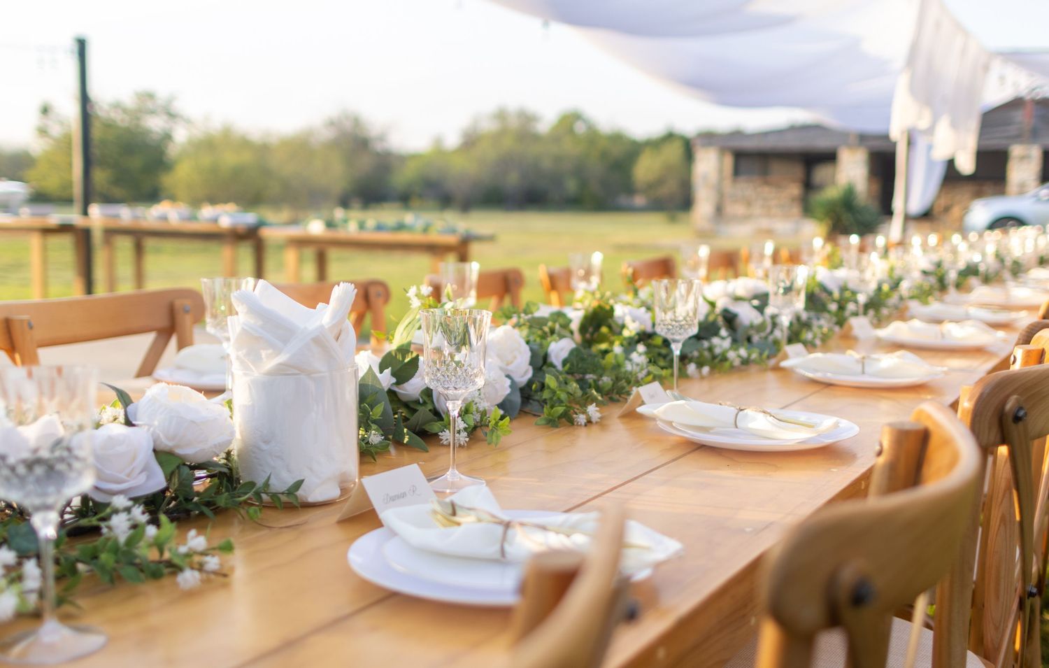 Long wooden reception table with white plates, greenery garland, and prairie views at a Grenville, Texas backyard wedding.