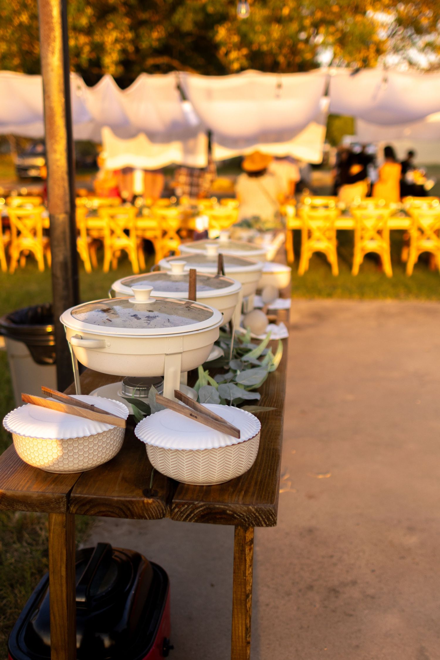 White ceramic mexican serving bowls arranged on rustic wooden tables at an outdoor backyard mexican wedding during golden hour lighting.