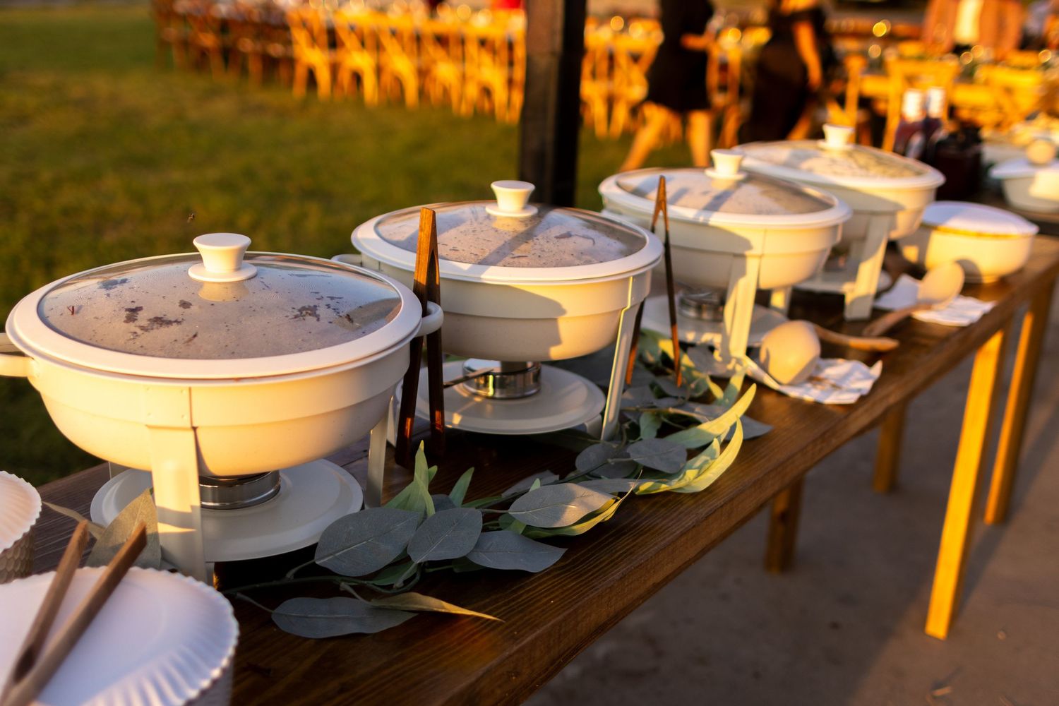 Outdoor wedding buffet setup at a Greenville Texas backyard wedding with chafing dishes and eucalyptus greenery during golden hour.