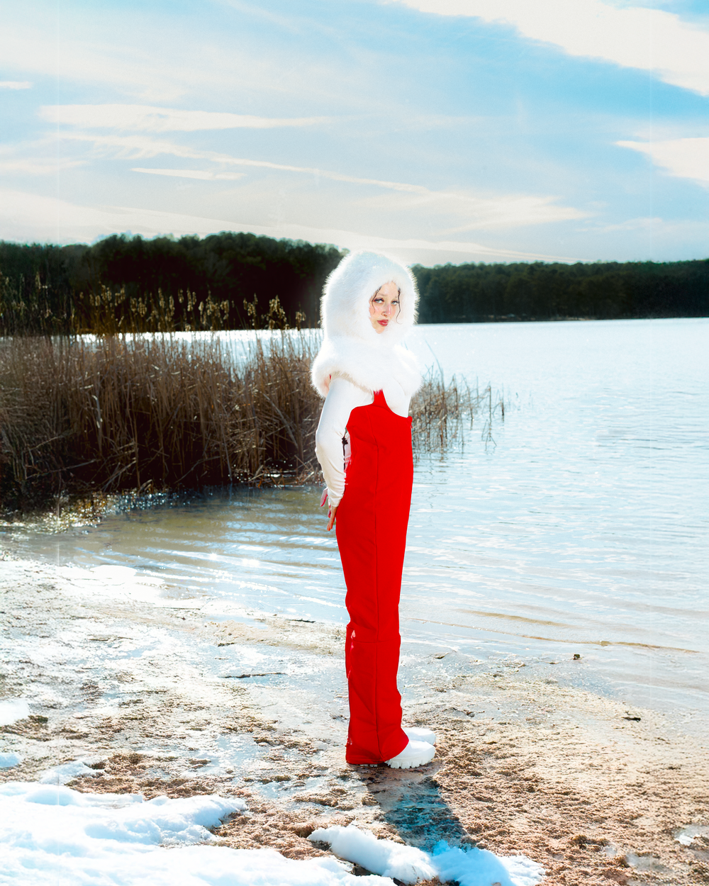 Figure in a striking red dress and white fur poses dramatically along a serene winter lakeshore.
