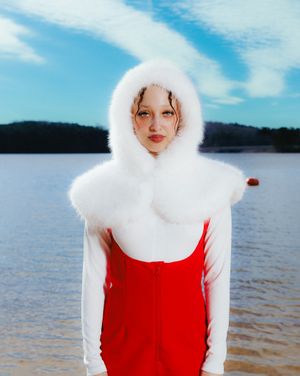 A person in a red dress and white fur hood poses on a snowy beach against a moody winter landscape.