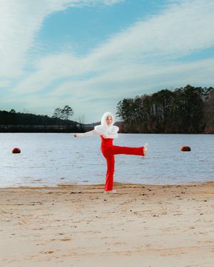 A sequence of photos showing a figure in red clothing performing a cartwheel motion on a sandy beach by a lake.