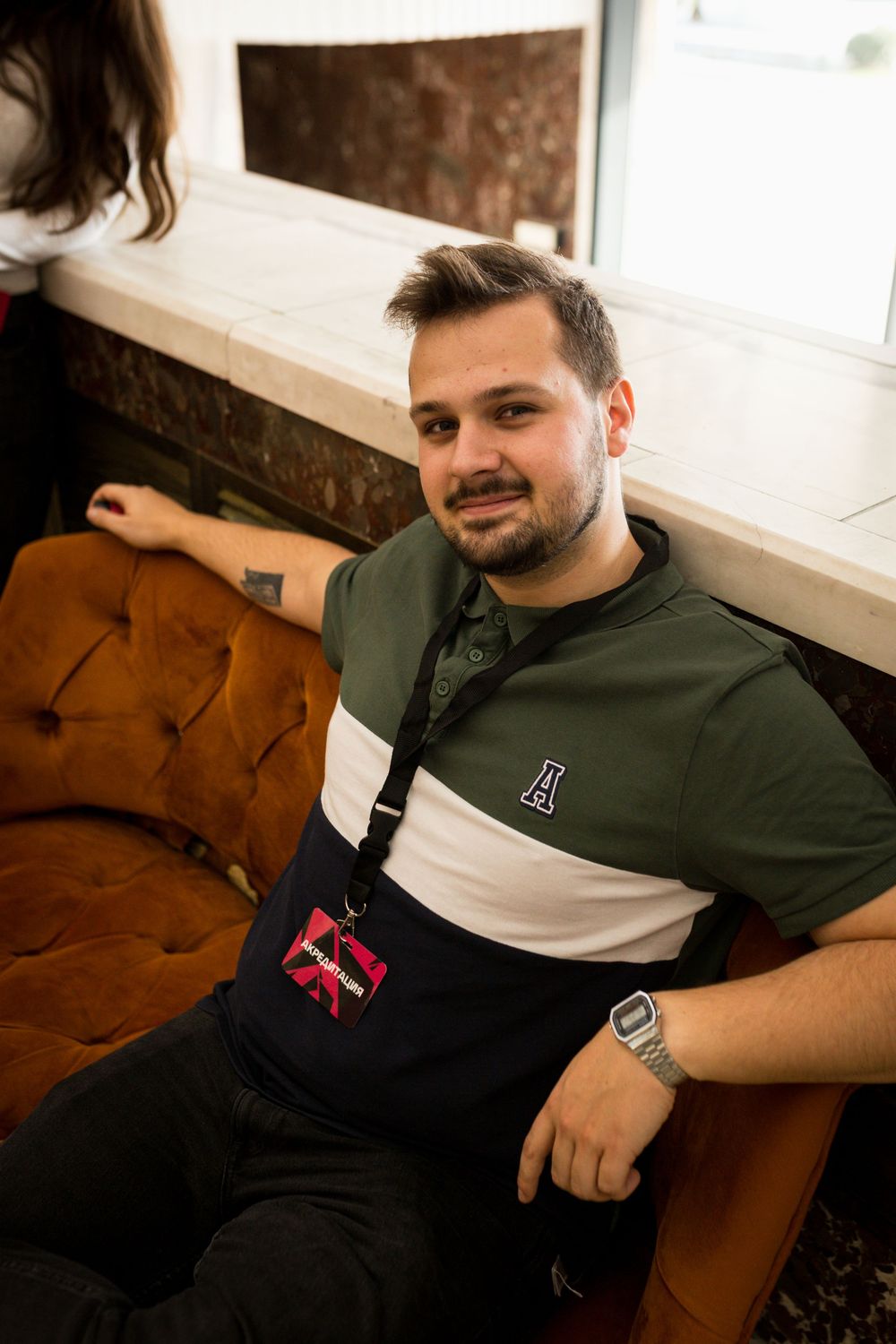 Smiling young man relaxing on orange velvet sofa in casual polo shirt.
