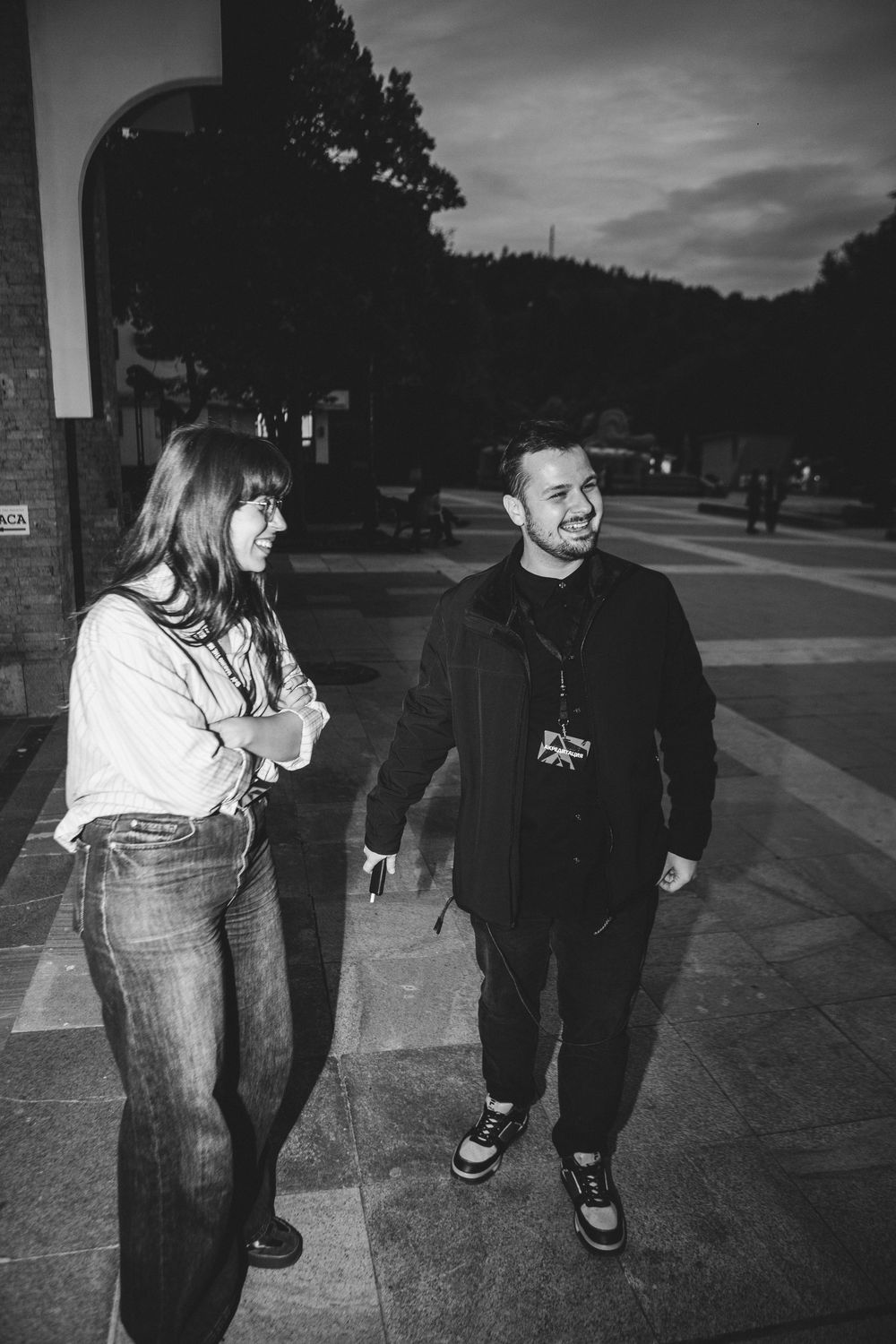 Man and woman walking together outdoors at dusk in black and white photo.