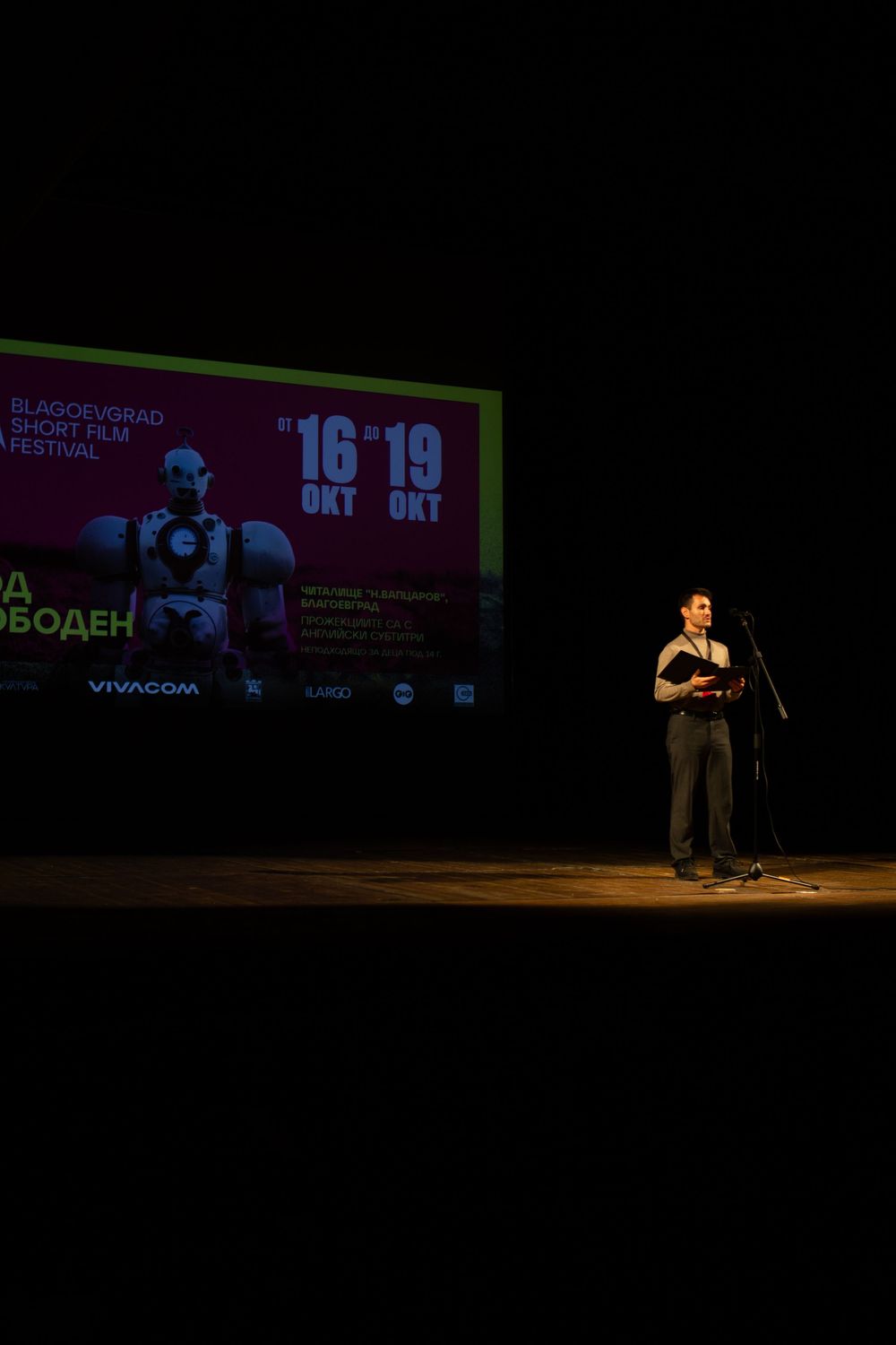 Speaker on stage at Blagoevgrad Short Film Festival with promotional screen backdrop.
