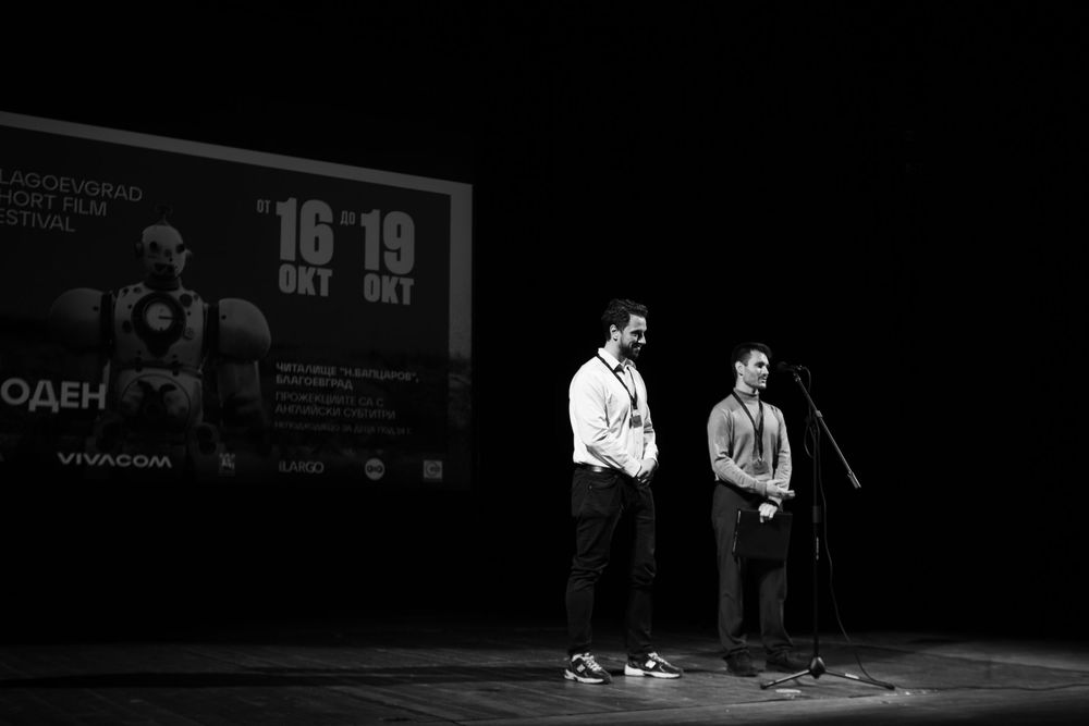 Two presenters on stage at Blagoevgrad Short Film Festival in black and white.