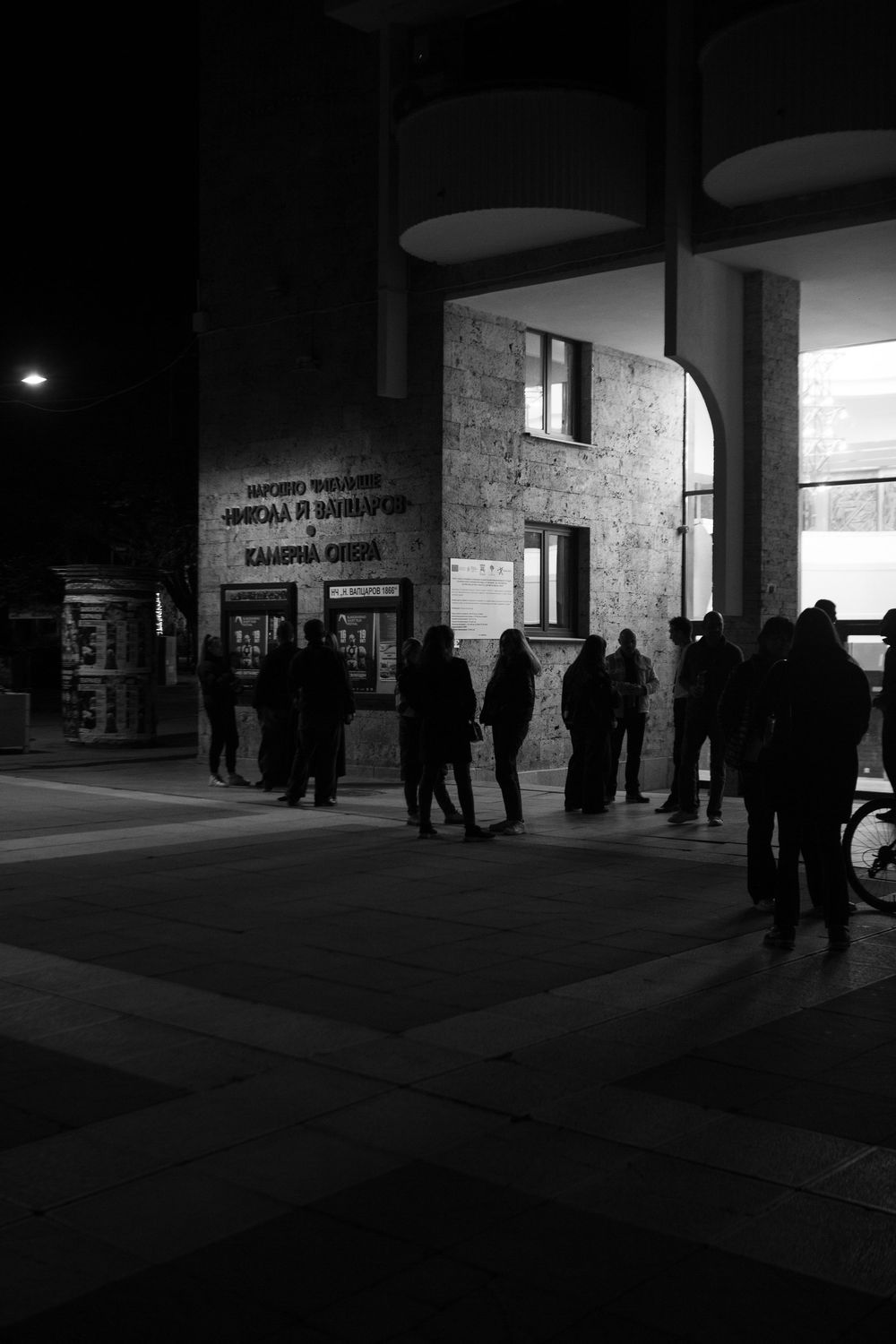 Black and white night shot of people gathered outside a theater building.