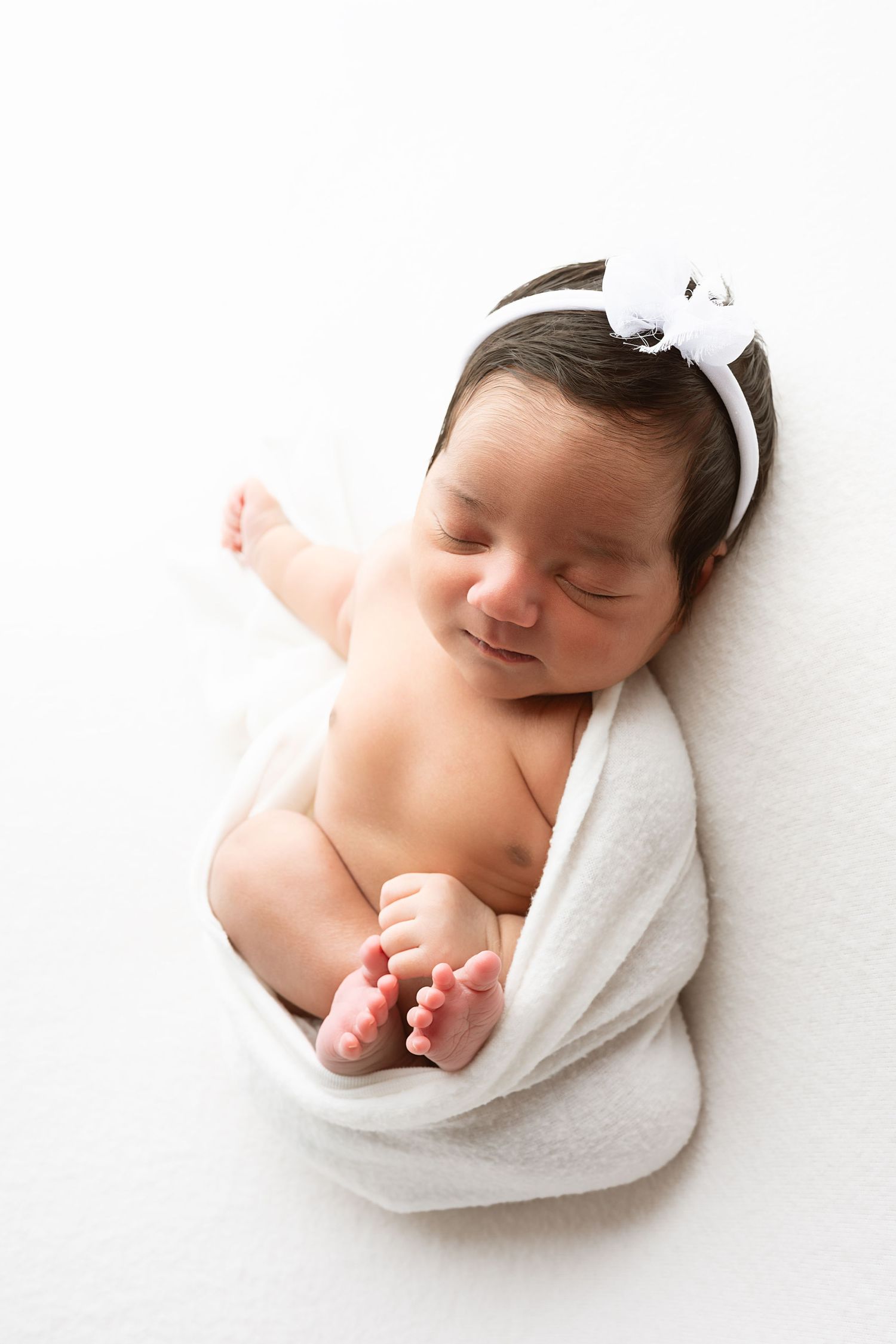 A sleeping newborn baby wrapped in soft white fabric against a white background in a series of three photos.