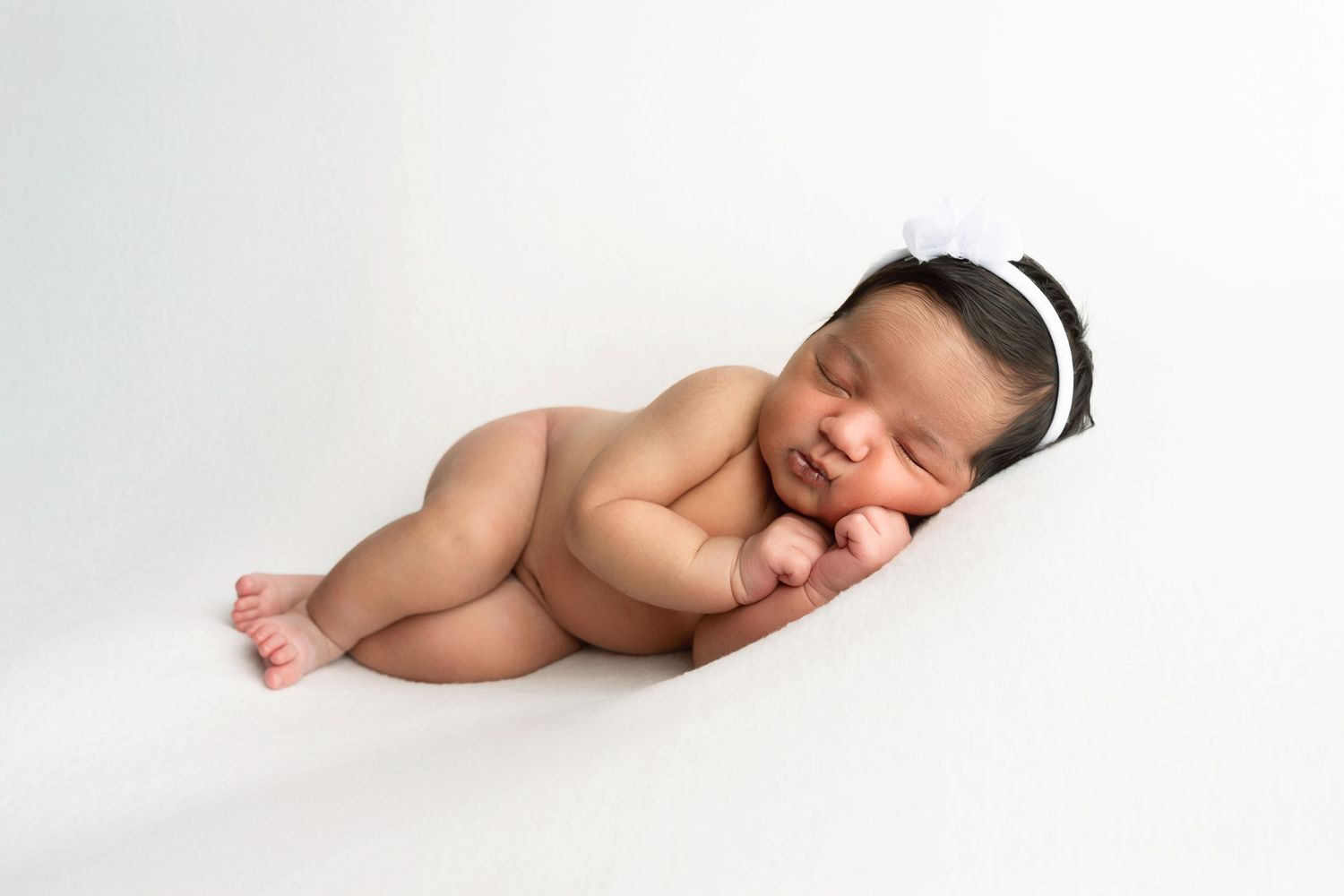 A sleeping newborn baby lies on a white blanket in a peaceful pose.