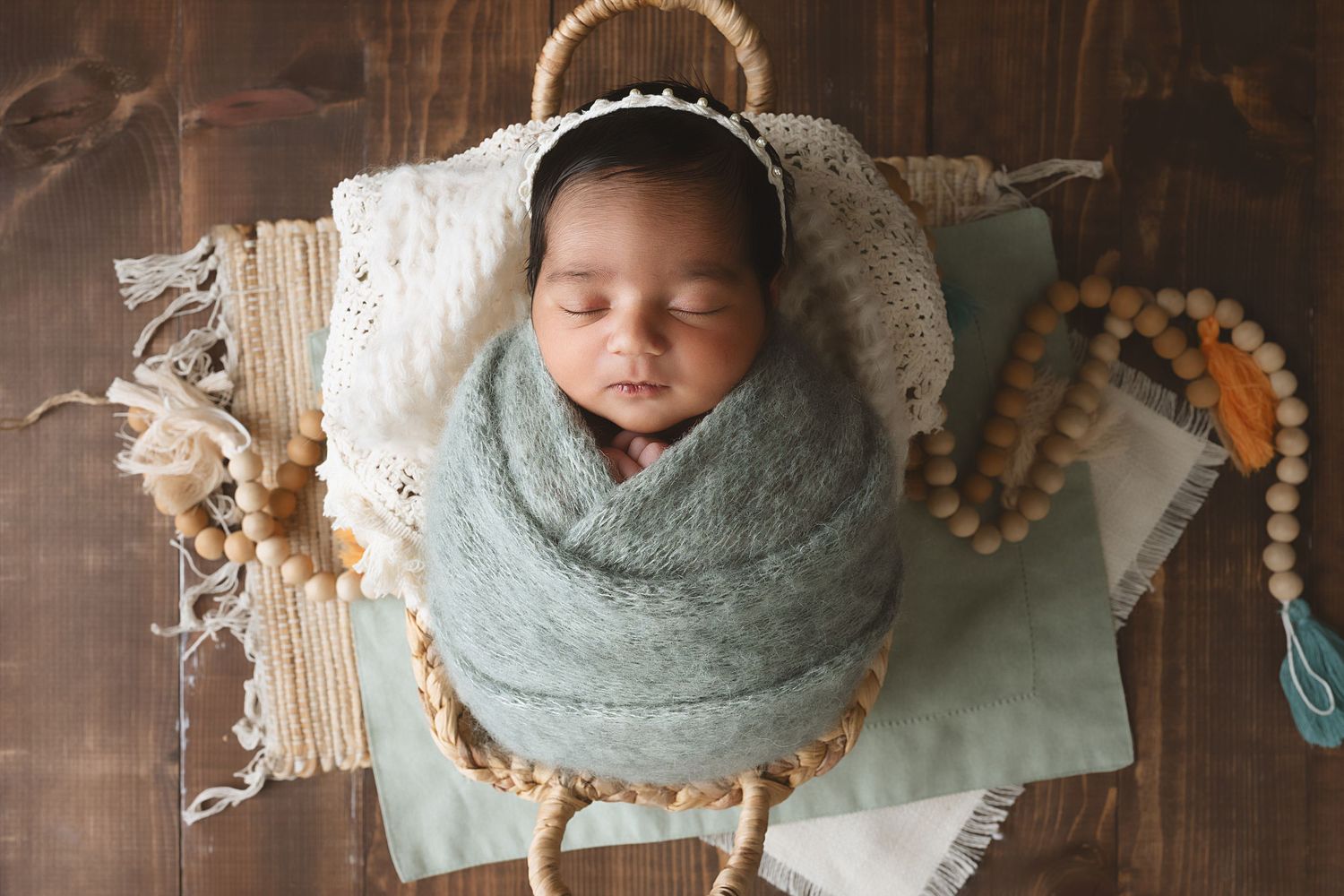 Newborn baby wrapped in soft mint green swaddle blanket during professional photography session.
