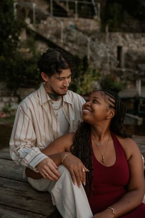 A romantic couple sits together on wooden steps at dusk sharing an intimate moment in warm lighting.