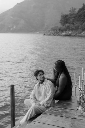 A couple shares a romantic moment on a wooden dock overlooking a serene lake and mountains.