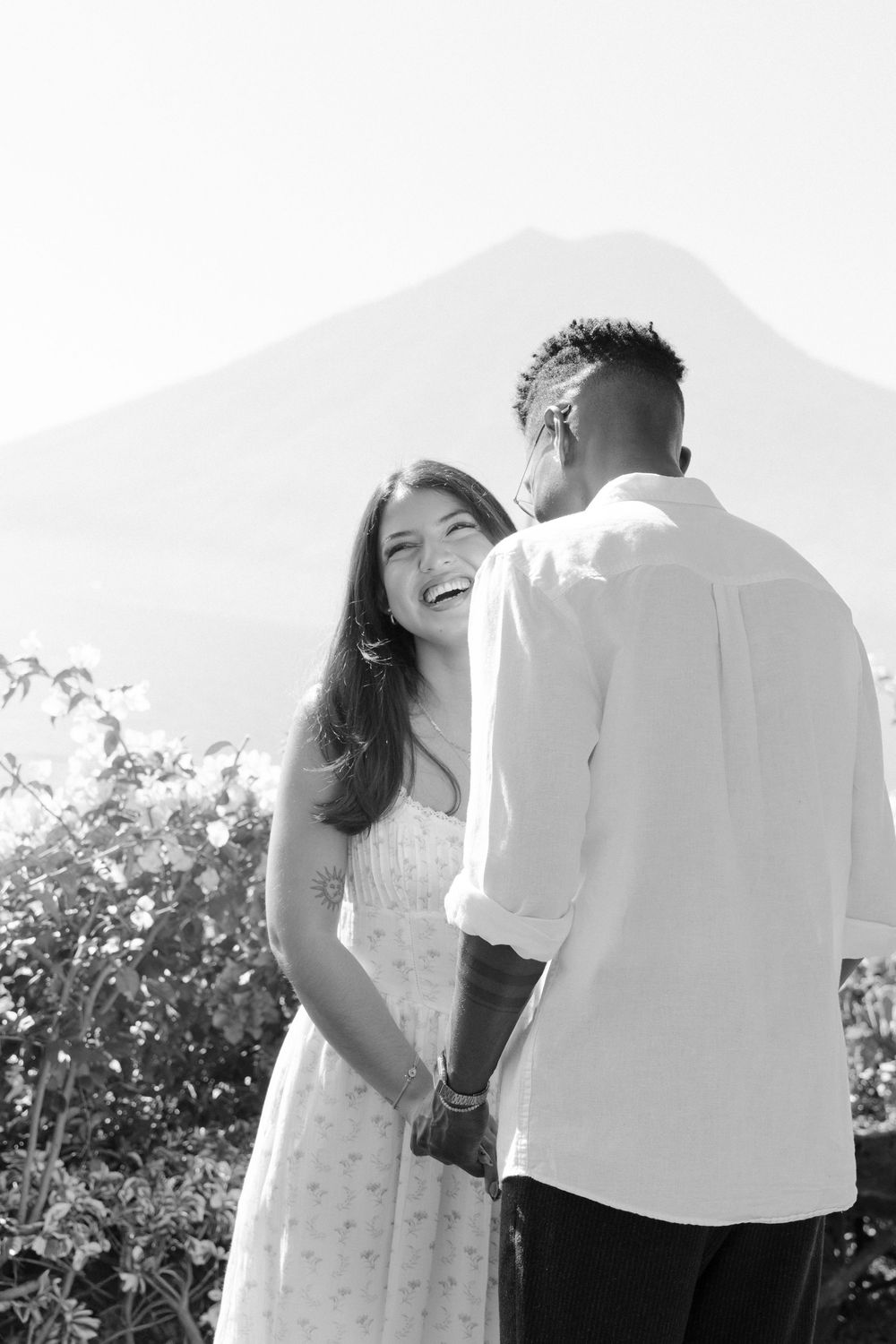 A joyful couple sharing a candid moment together outdoors in bright sunlight wearing white clothing.