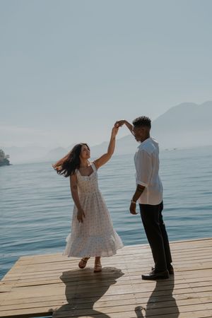 A couple dances playfully on a wooden dock by the ocean during a serene afternoon.