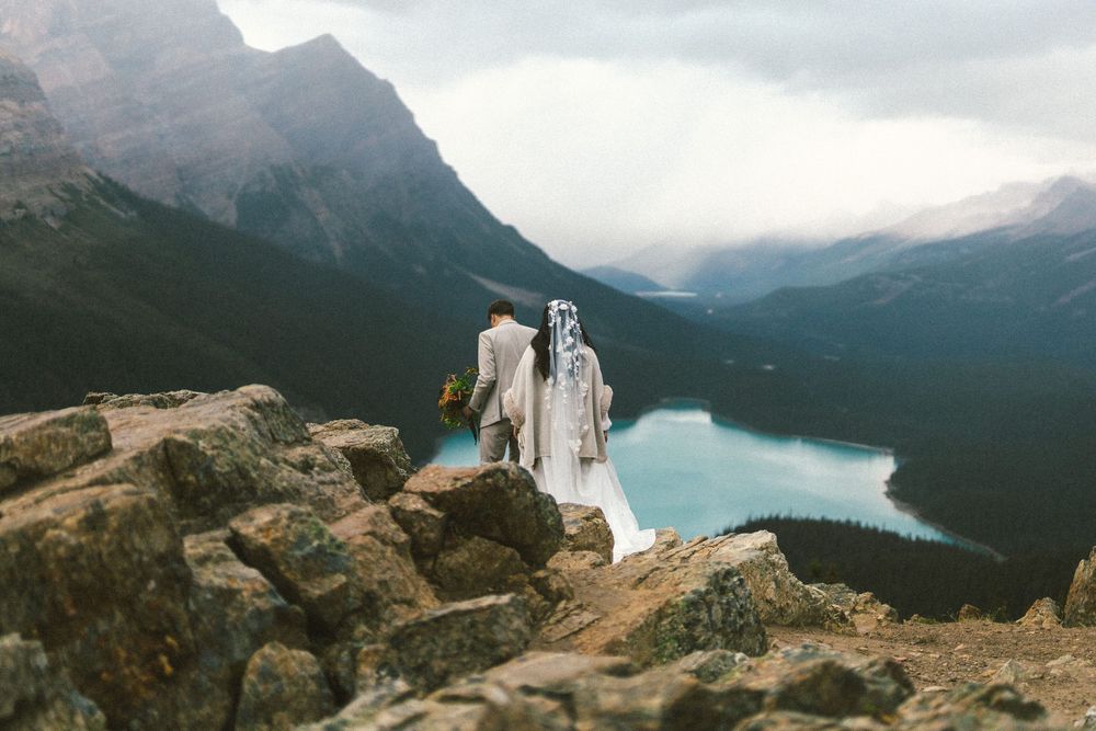 bride and groom walk along rocks at Peyto Lake in Banff