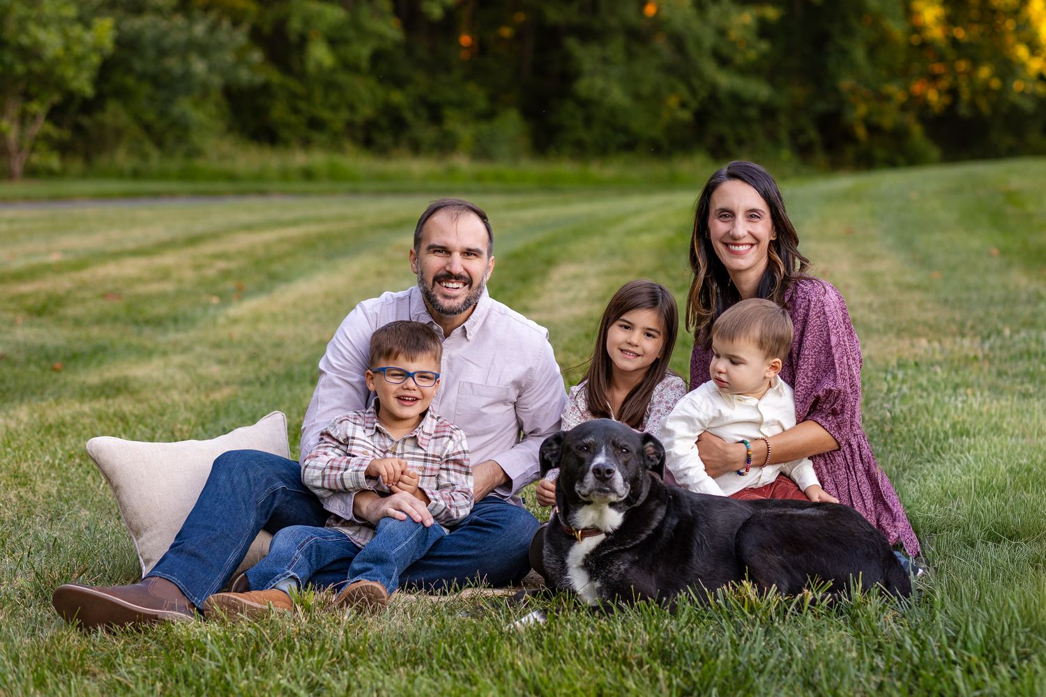 People lounging on grass with their dog during a golden hour outdoor family photo session.