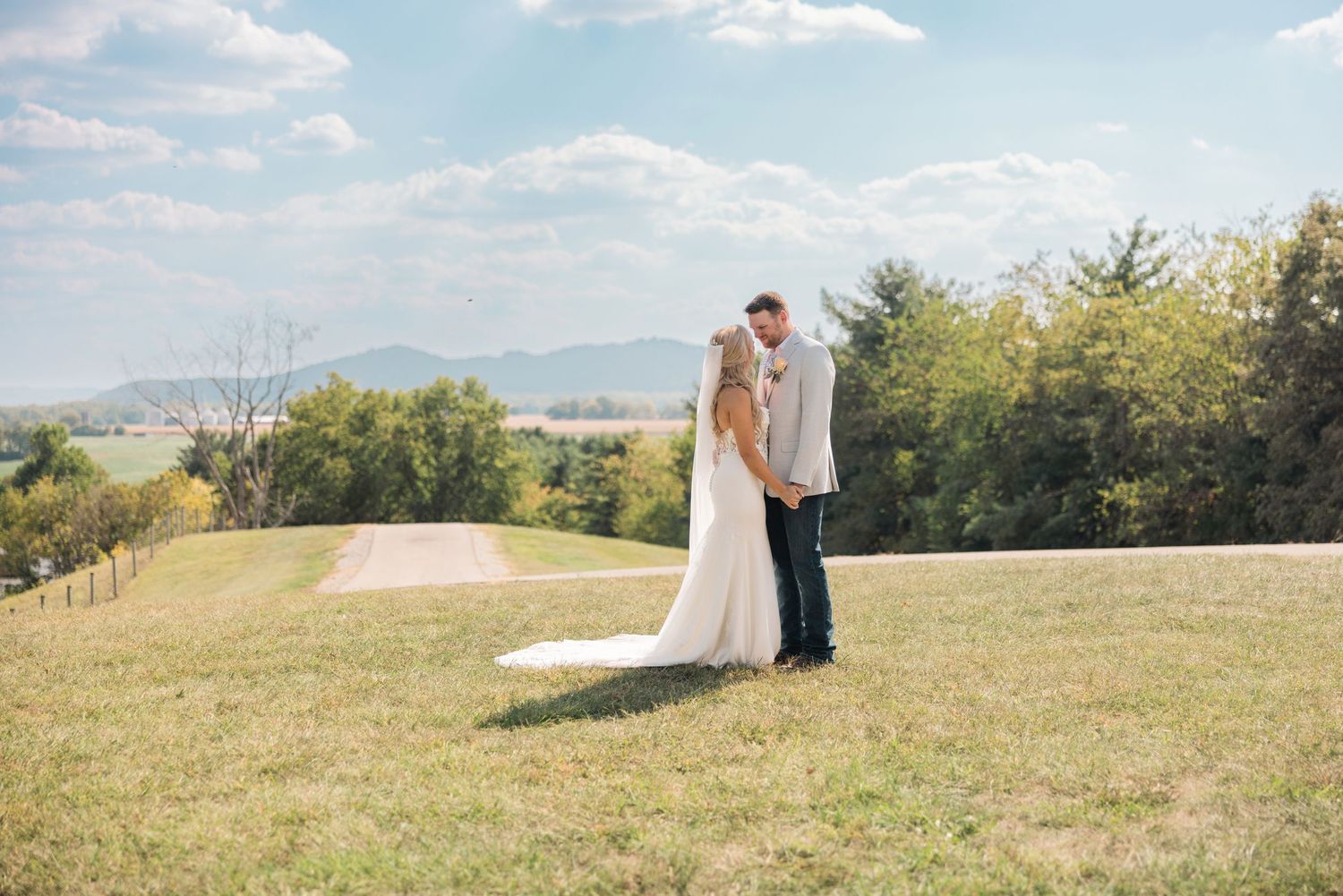 A scenic wedding photoshoot in a grassy field with a flowing white dress and veil against a blue sky backdrop. Bell Manor Chillicothe Ohio.