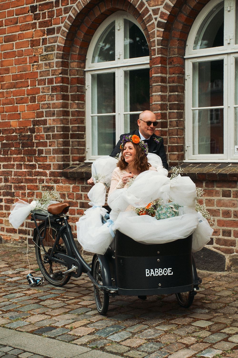 Three cargo bikes with white foam or bubbles parked in front of a historic brick building with arched windows.