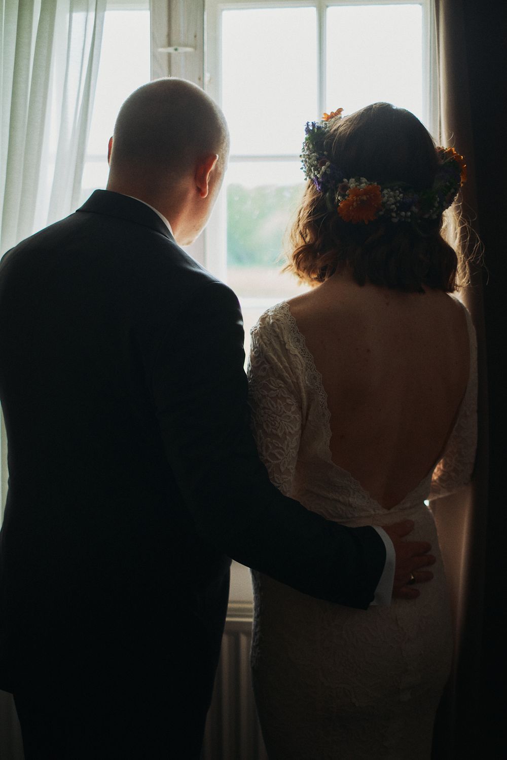 A silhouetted couple stands by large windows in a series of five connected romantic wedding photos.