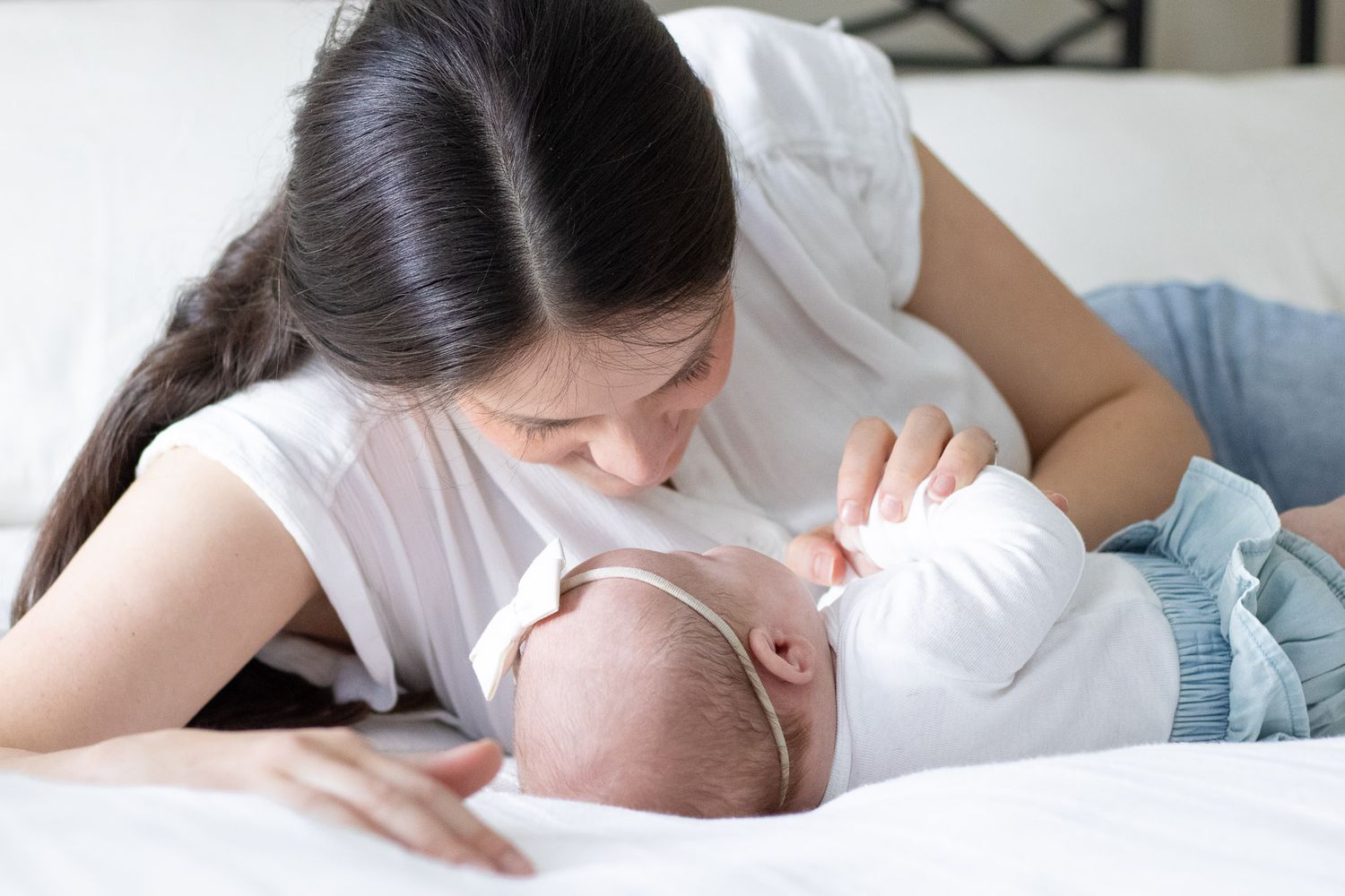 A mother lovingly nurtures her newborn baby while lying together on a soft bed.