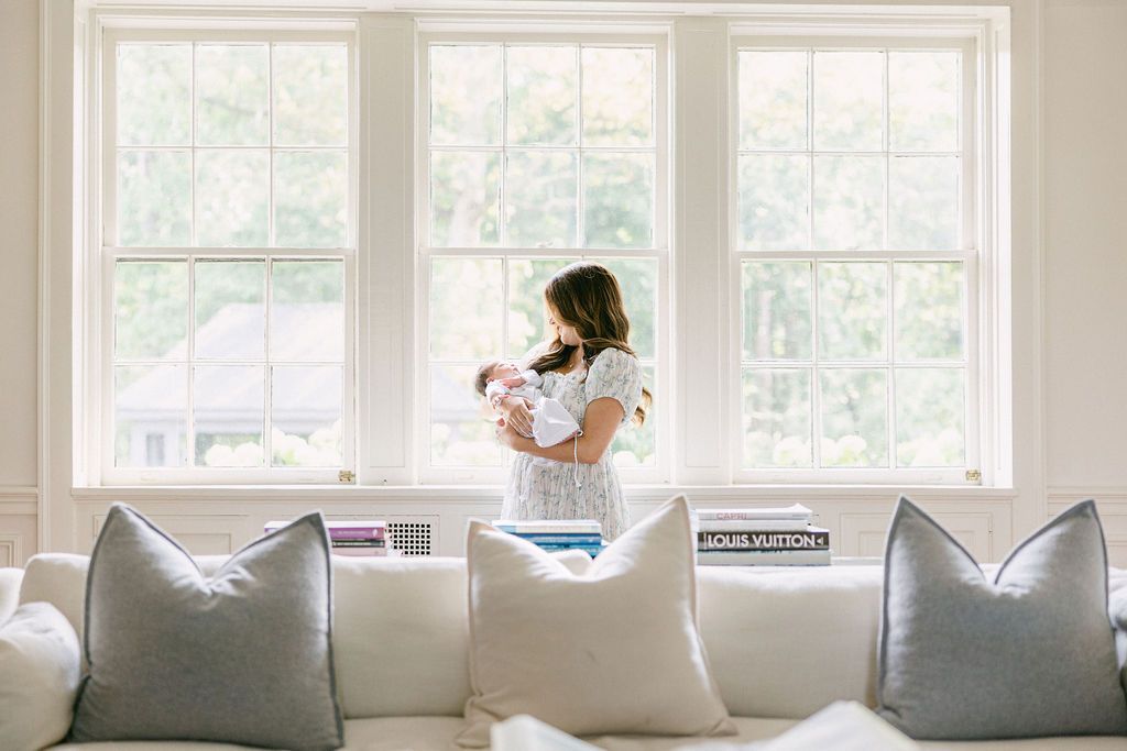 A bright, airy living room features white walls, large windows, and light gray throw pillows arranged on a white couch. In-home photography