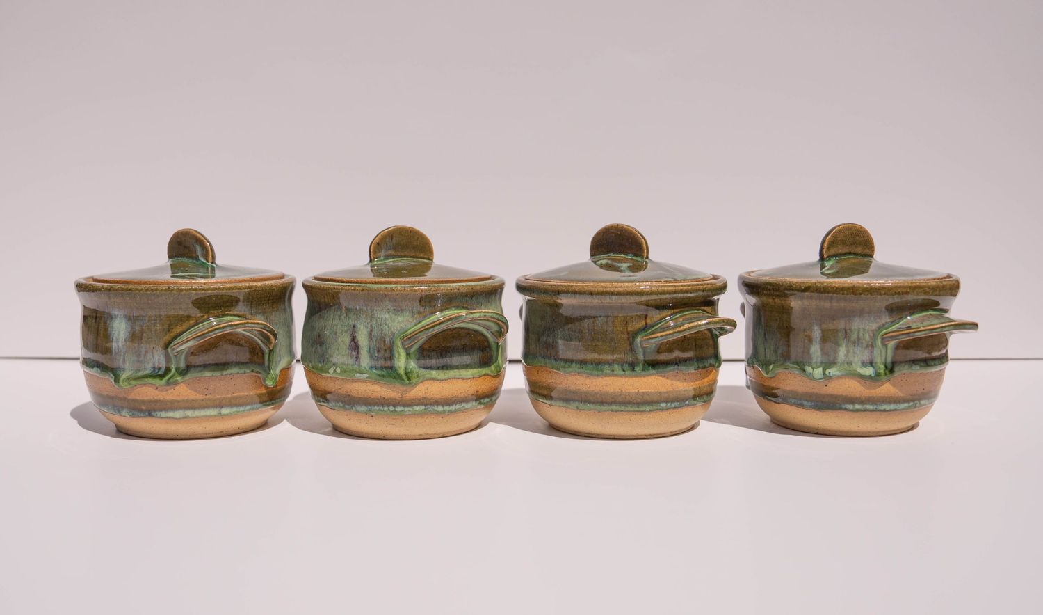 Set of four handcrafted green and brown glazed ceramic lidded pottery jars with decorative handles.