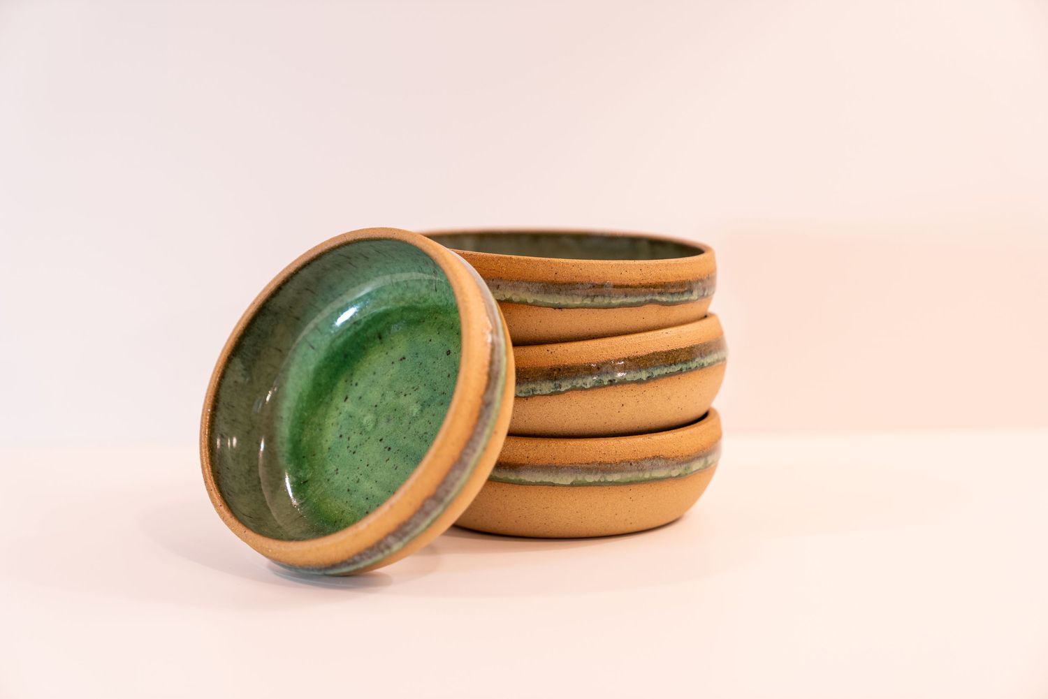 Stack of handmade ceramic bowls with green interior glaze and natural sandy exterior on a white background.