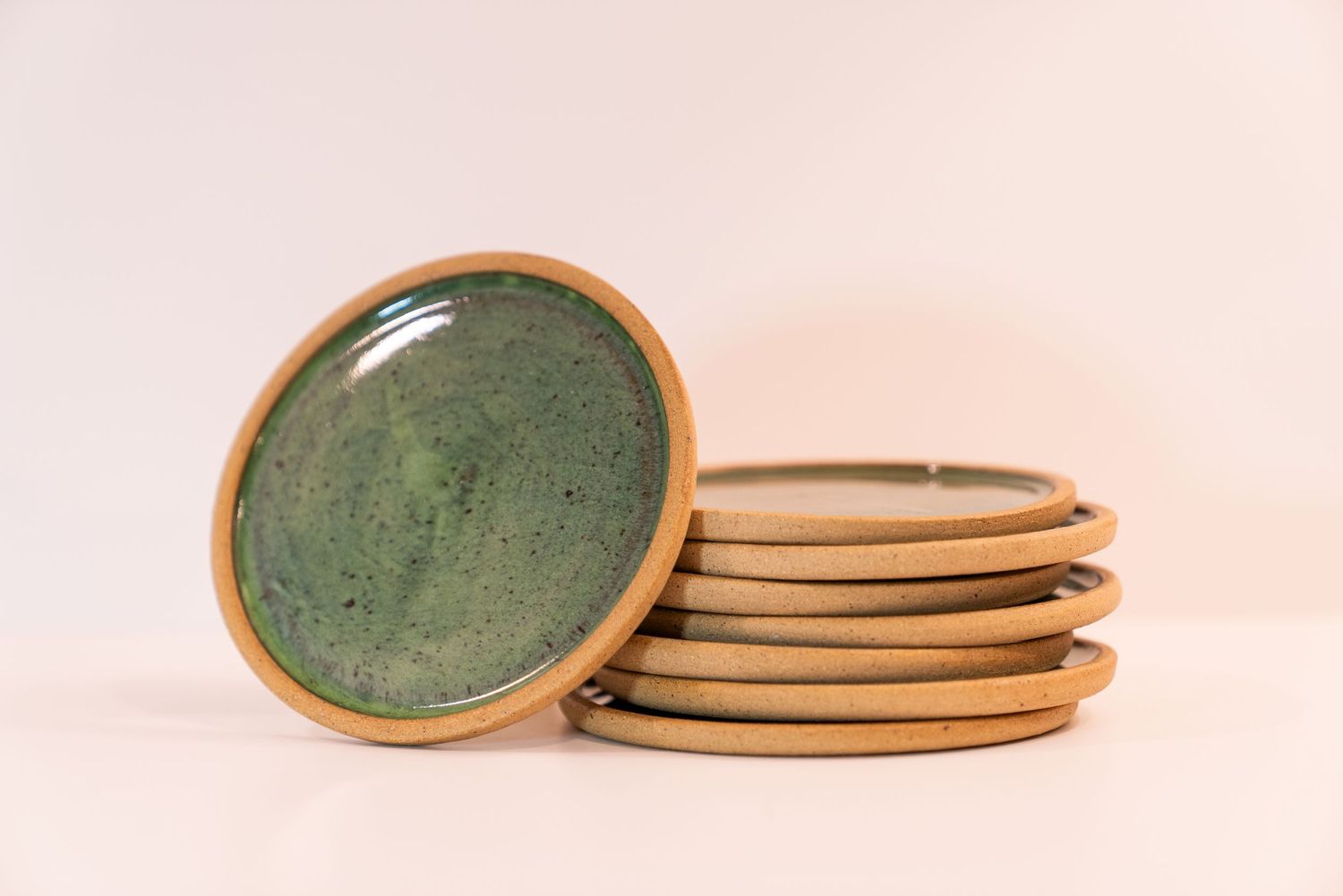 Stacked handmade ceramic plates with green speckled glaze and unglazed sandy rim on a white background.