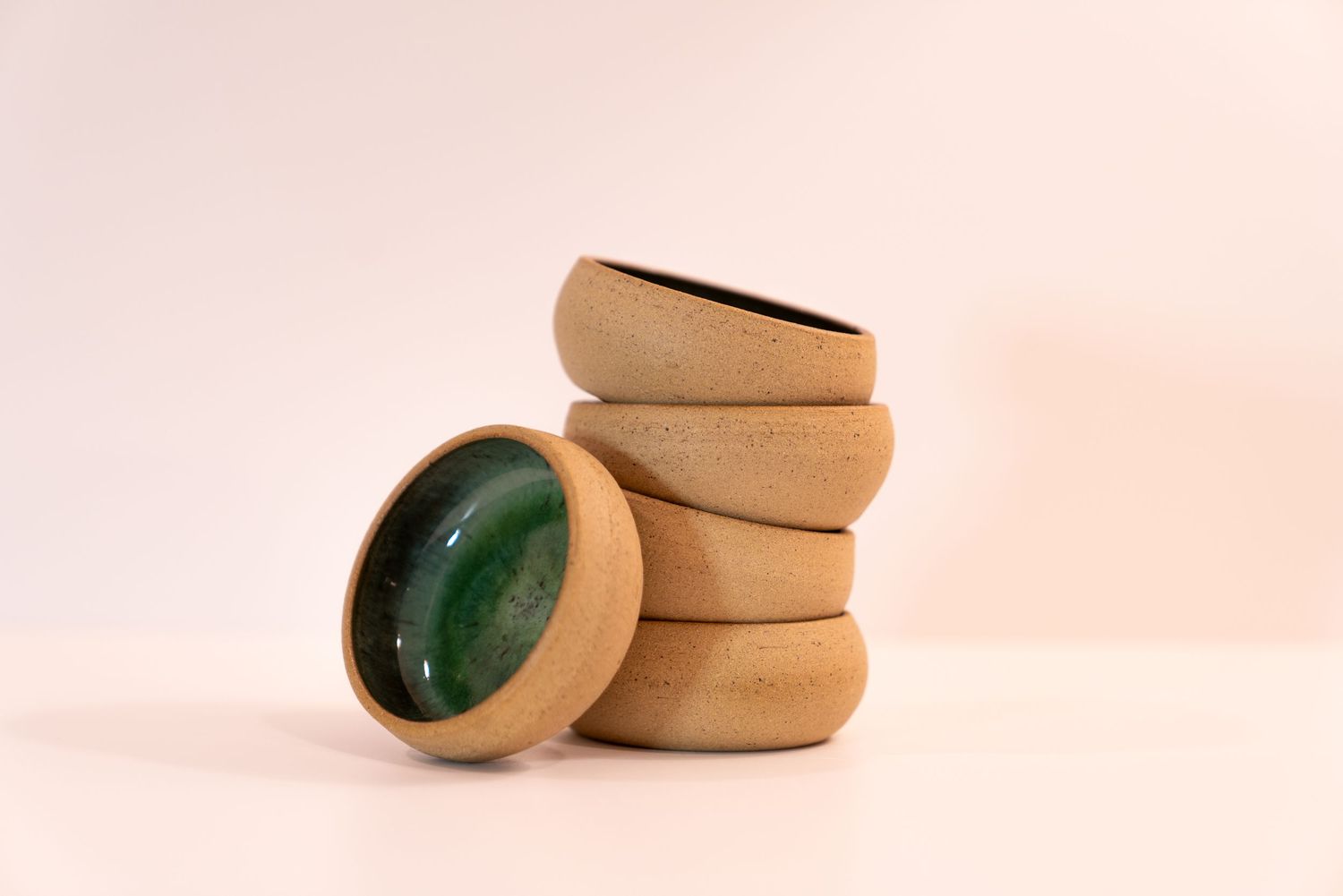 Stack of handmade ceramic bowls with deep green interior glaze and natural unglazed exterior on a white background.