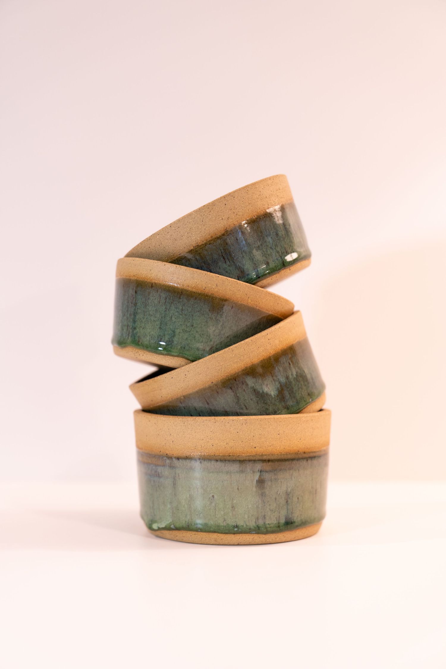 Stack of four handmade ceramic bowls with deep green interior glaze and unglazed sandy exterior on white background.