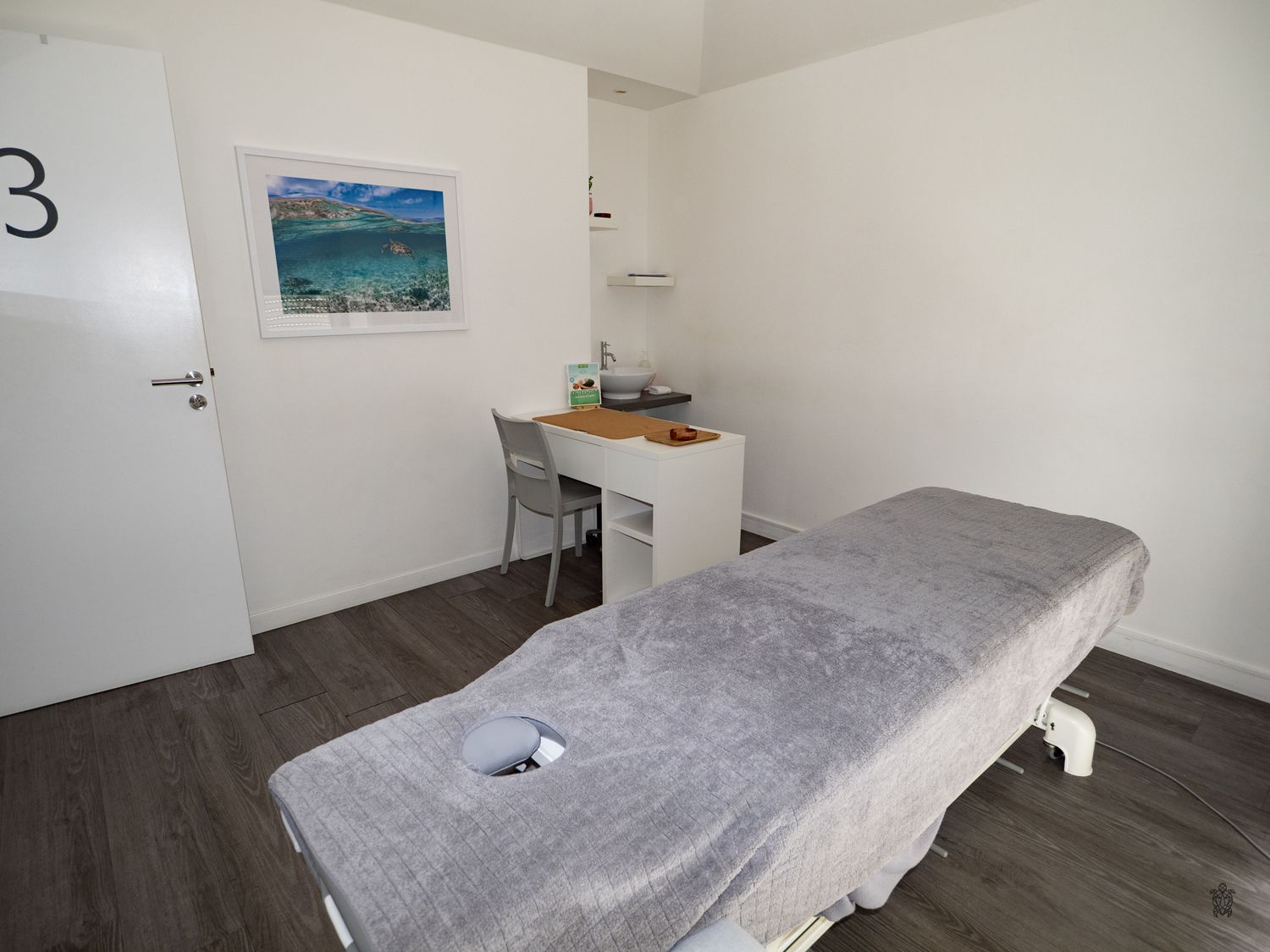 Modern bedroom interior with gray bedding, dark wood flooring, and white walls in a minimalist style.