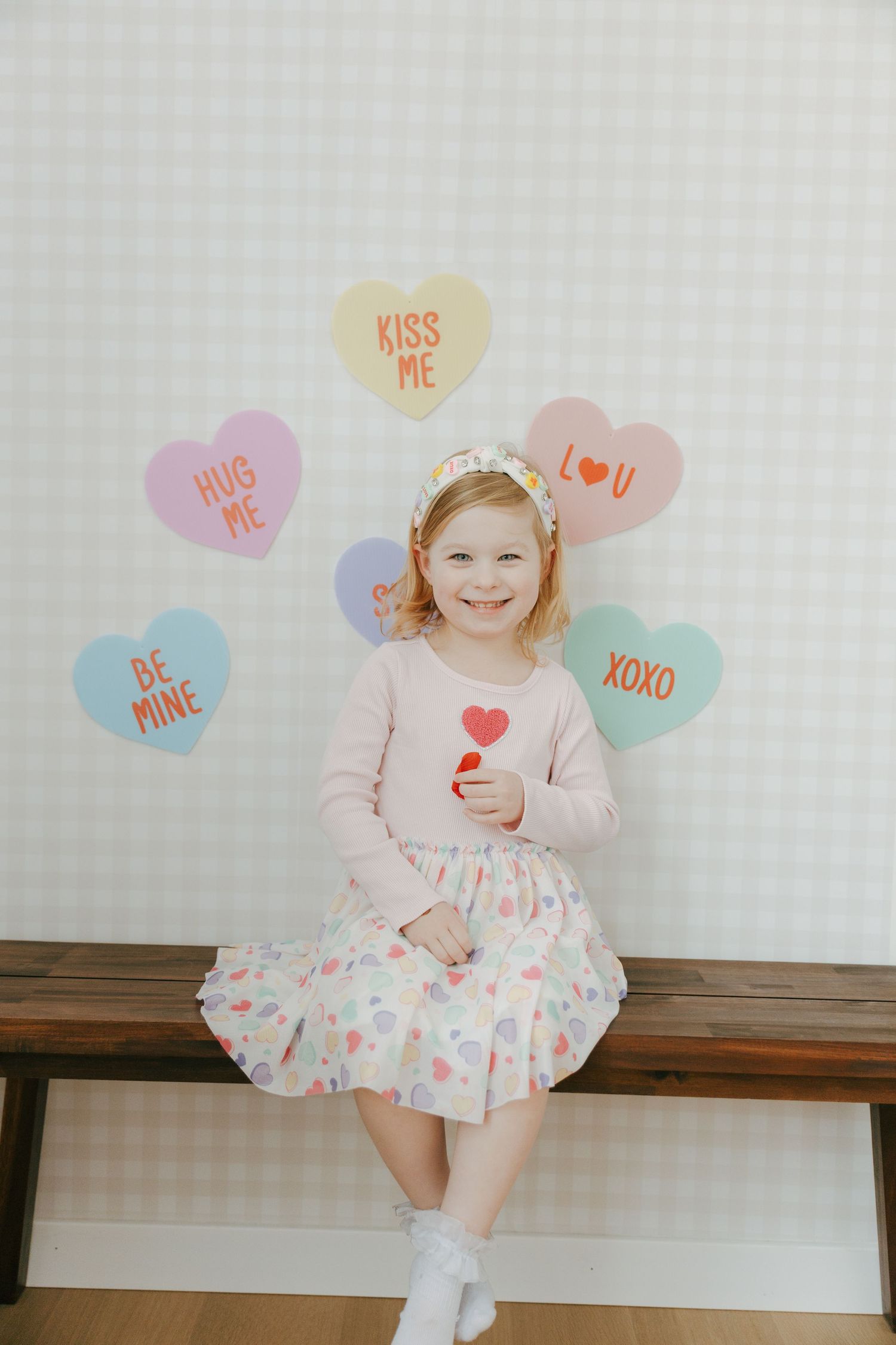 Valentine's Day themed photo series with conversation heart decorations and a pink dress against a white wall.