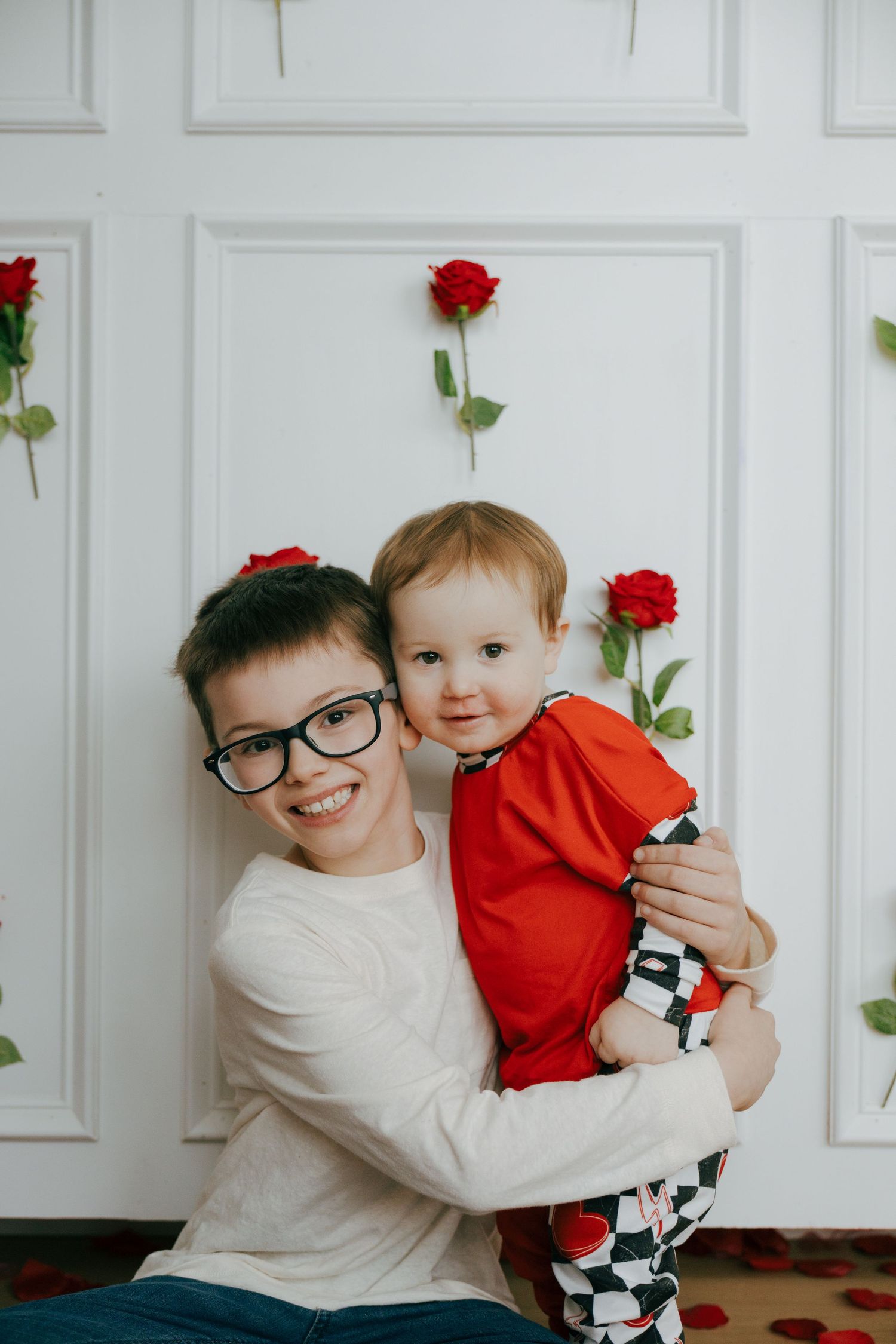 A heartwarming family photoshoot against a white wall decorated with red roses.
