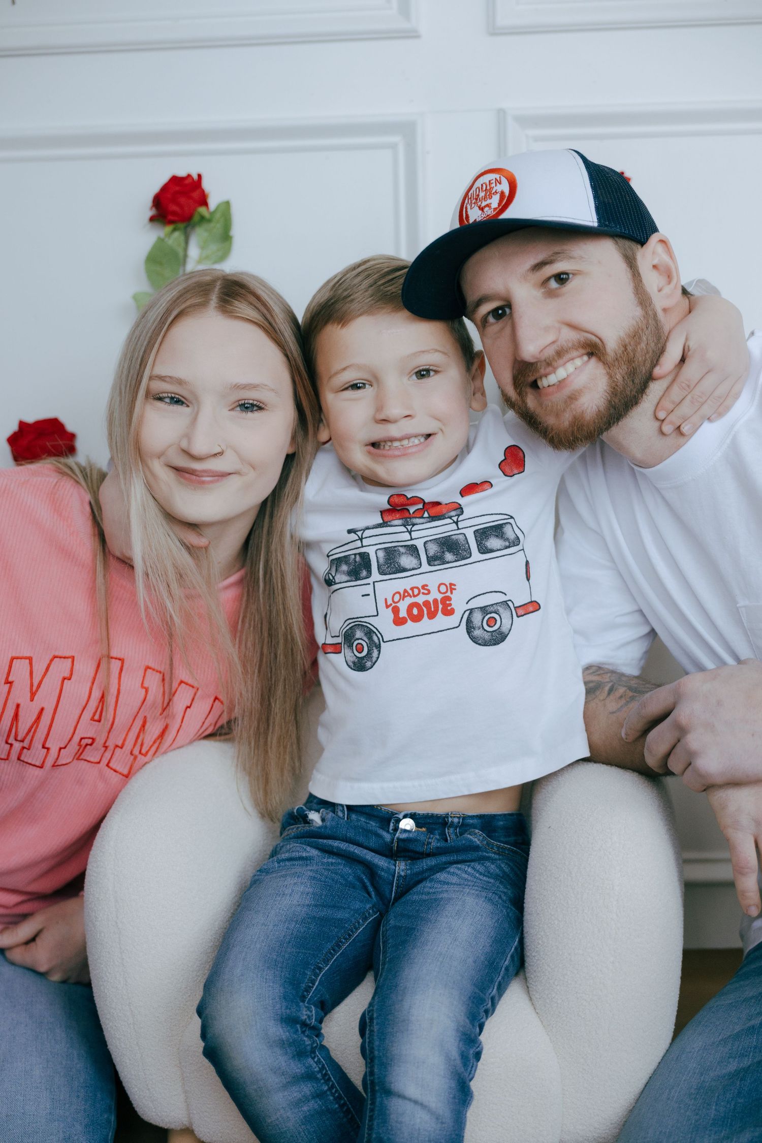 A family wearing casual clothes poses together against a white door, with the child wearing a t-shirt featuring a van design.