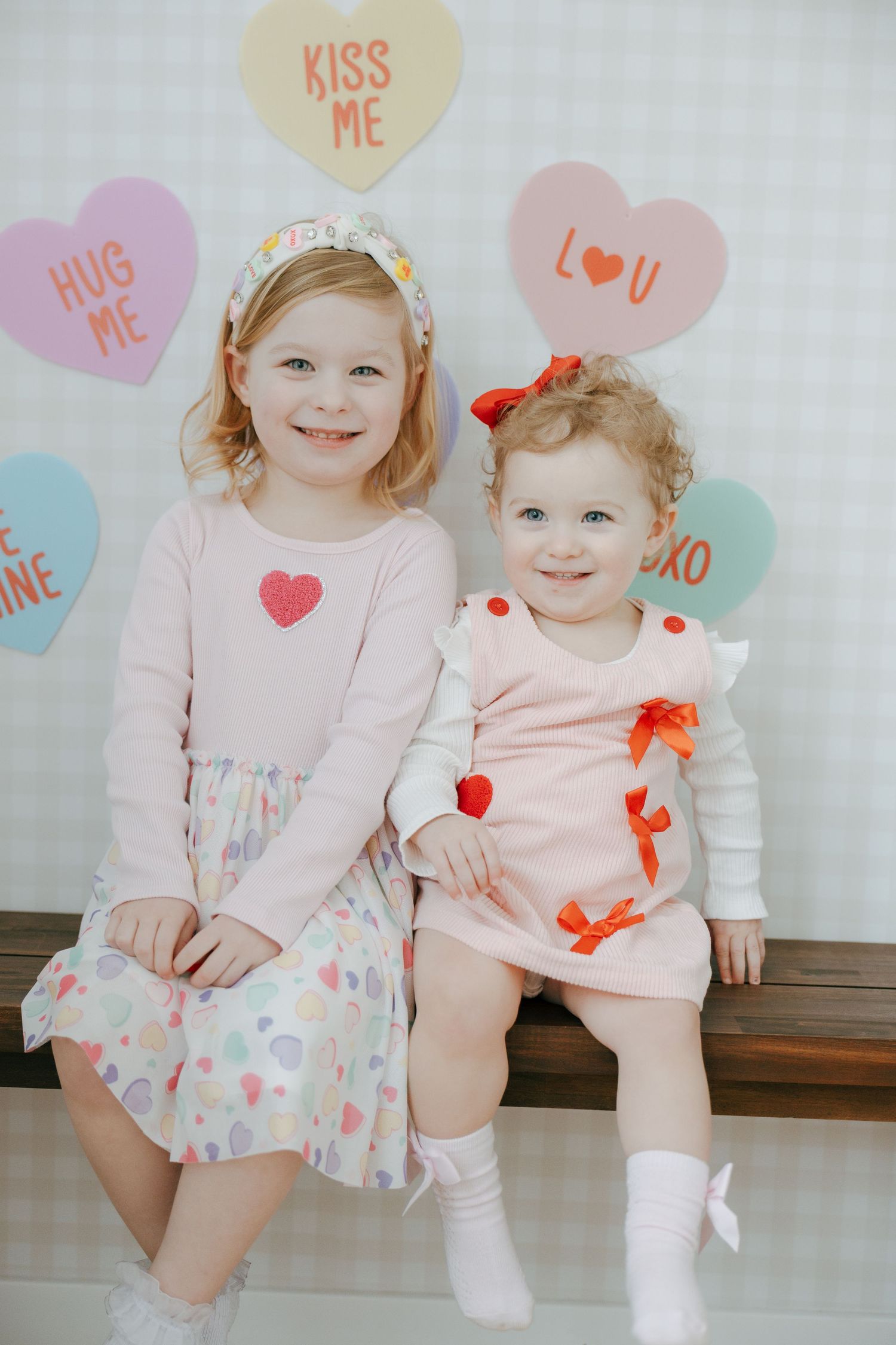 Sweet Valentine's themed photo with heart decorations and two children wearing pink outfits sitting on a bench.