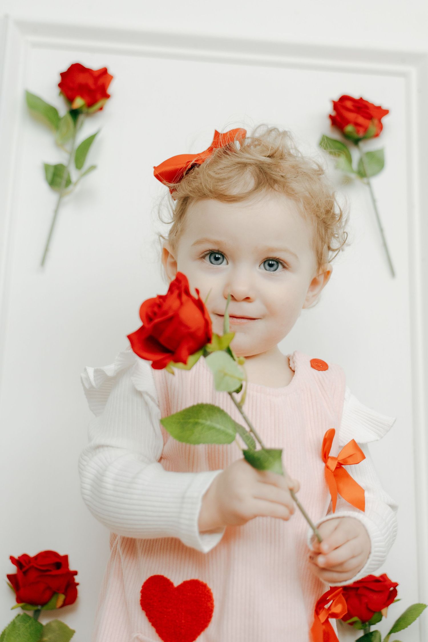 Sweet baby in white dress poses with vibrant red roses against white backdrop in artistic photo collage.