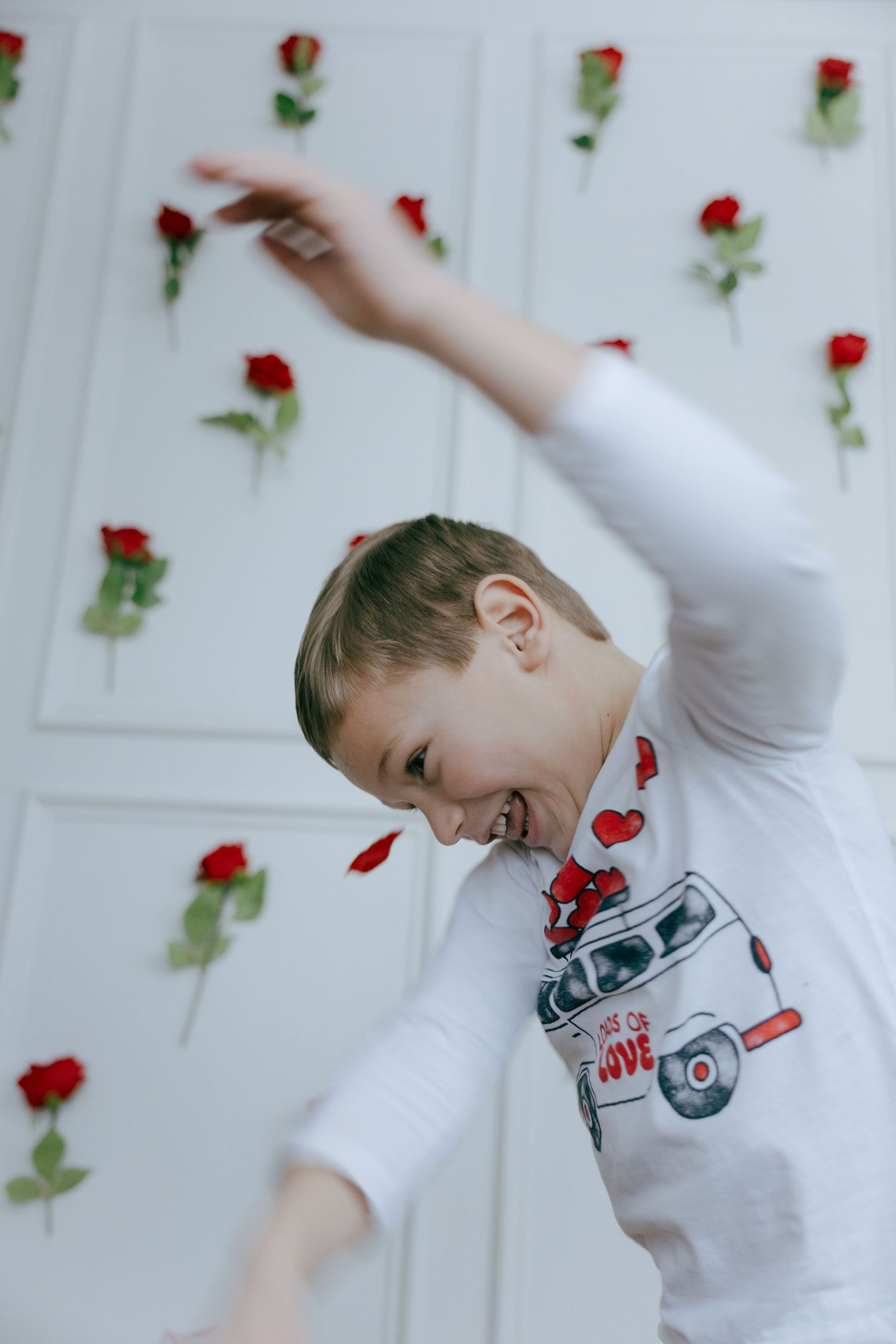 A young dancer in a white shirt with a car design twirls gracefully against a floral backdrop of red roses.