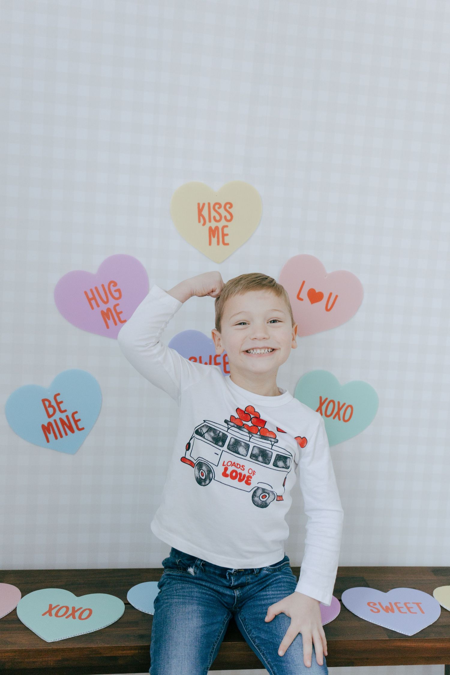 Valentines themed photo series with candy heart decorations and a white shirt with love bus design against gray backdrop.