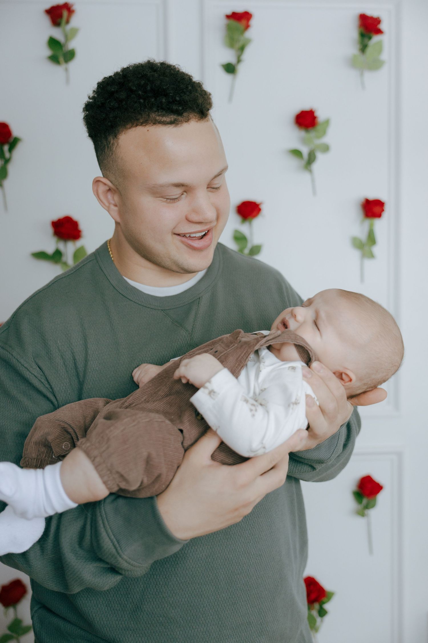 A tender moment between parent and baby in a white room decorated with red roses on the wall.
