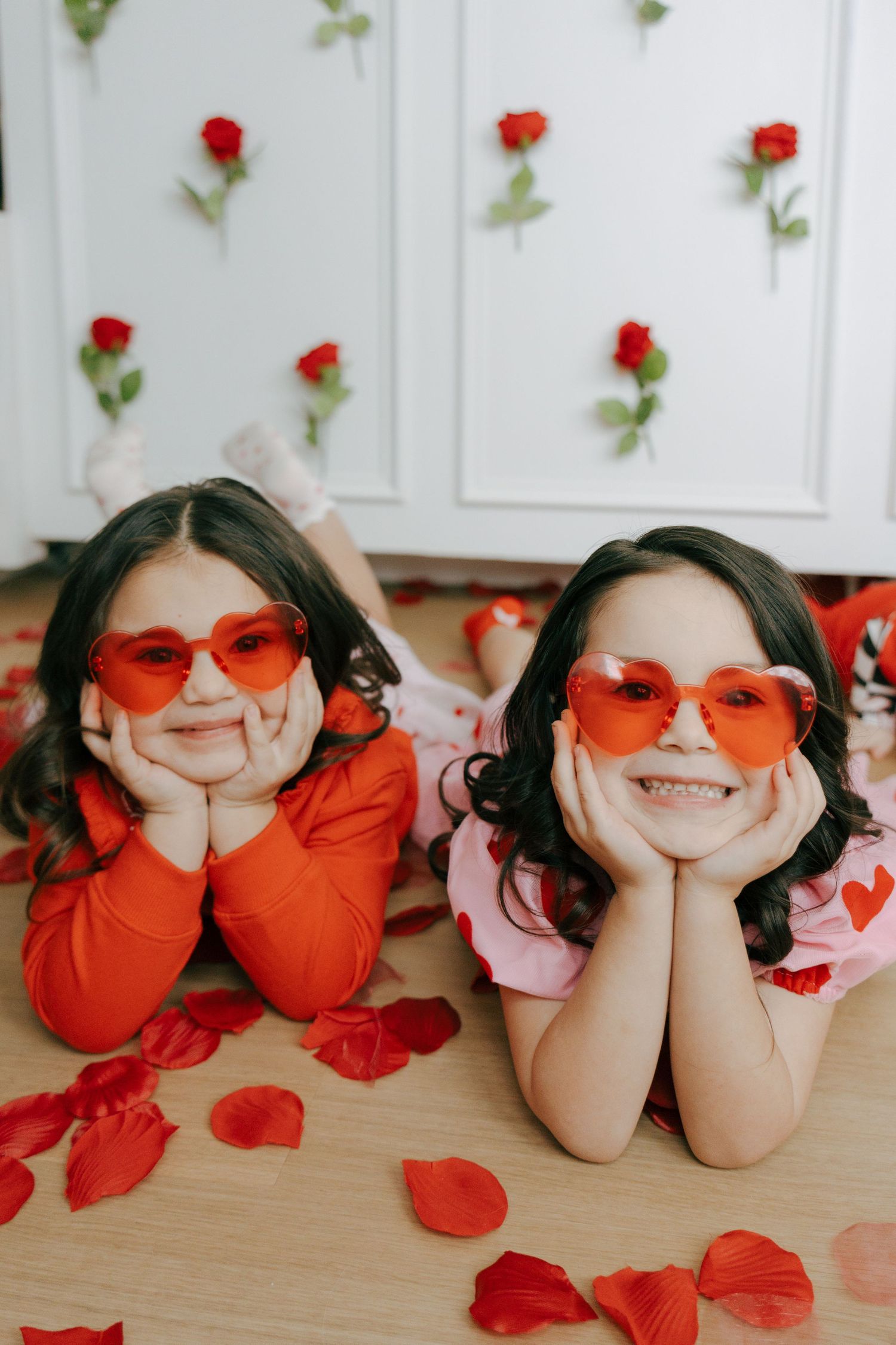 A playful Valentine's Day themed photoshoot with red heart-shaped glasses and rose petals on wooden floor.