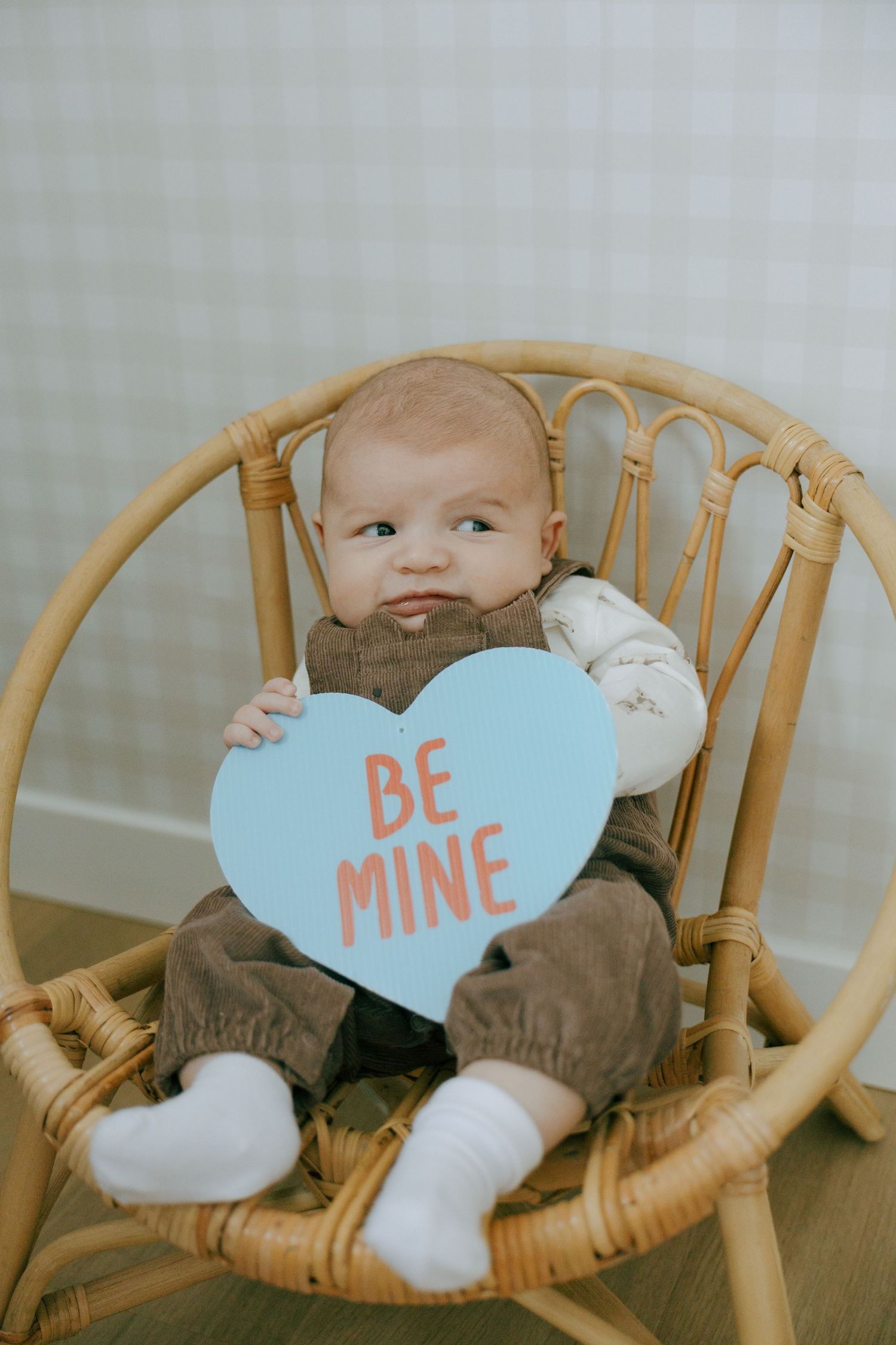 A series of four photos showing a baby in a wooden chair with blue heart-shaped Valentine's Day message cards.