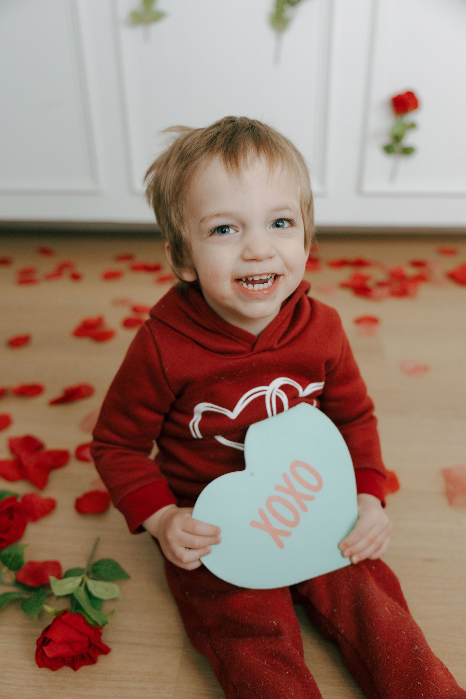 A series of Valentine's Day photos showing someone in a red sweater holding light blue heart-shaped cards with red rose petals.