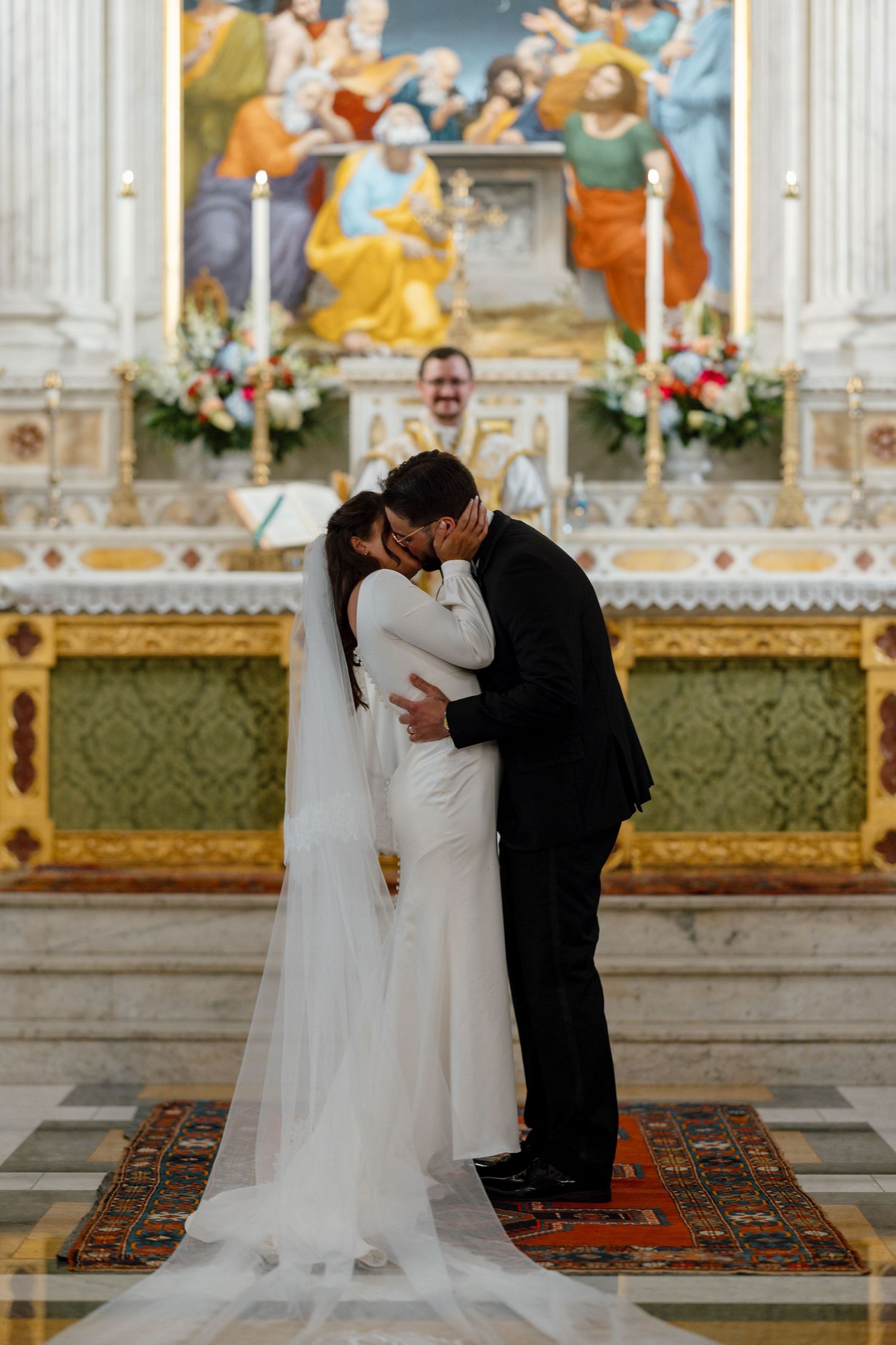 A wedding couple shares a tender moment during their ceremony in an ornate church with gilded details and a decorative carpet.