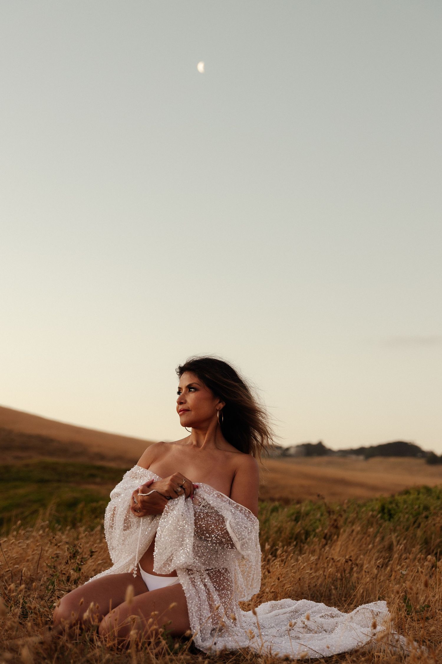Woman in white lace dress lies gracefully in golden field during sunset.