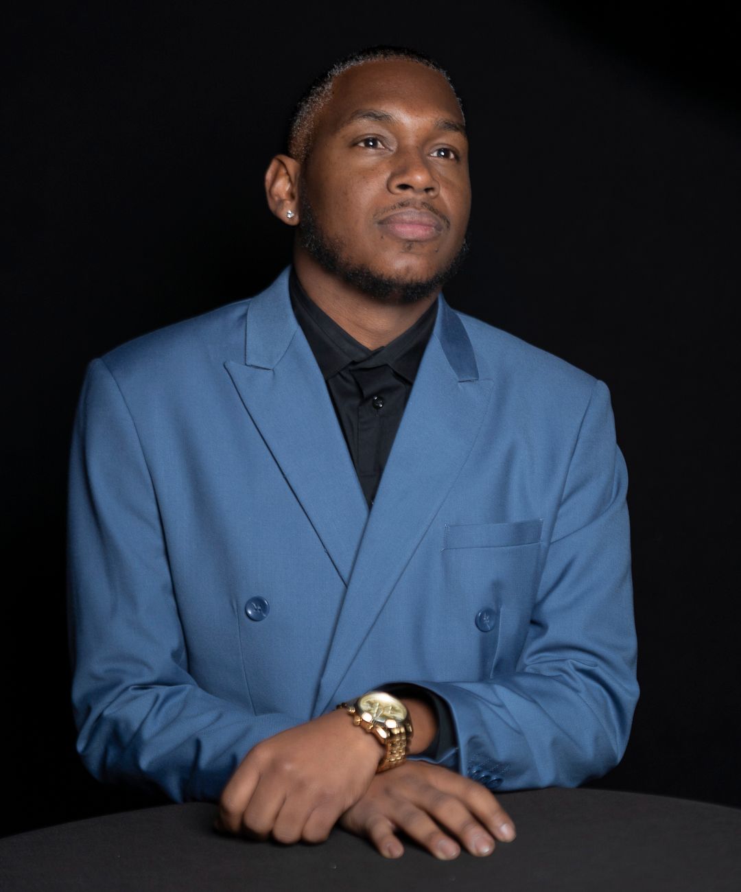 Professional headshots of a person wearing a light blue blazer and black shirt against dark background.