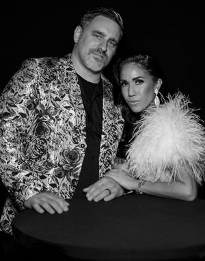 Couple in formal wear with floral jacket and feathered dress posing for black and white photo.